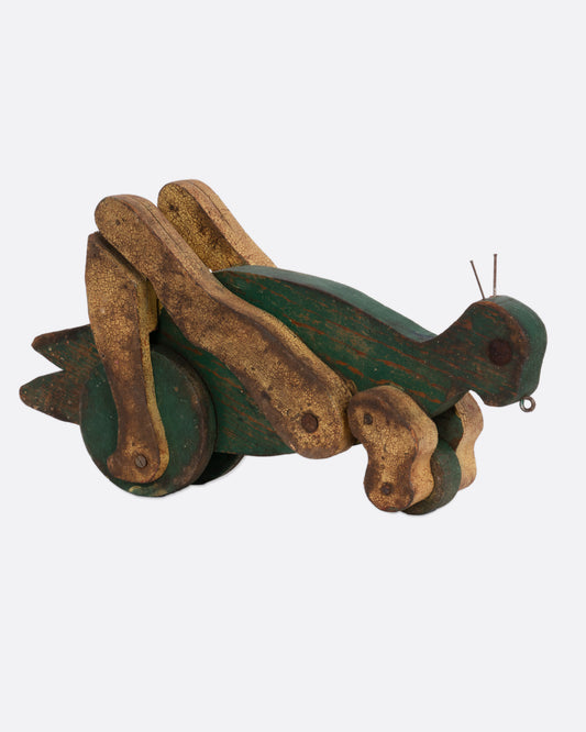 A green wooden articulated grasshopper toy, shown from the side.