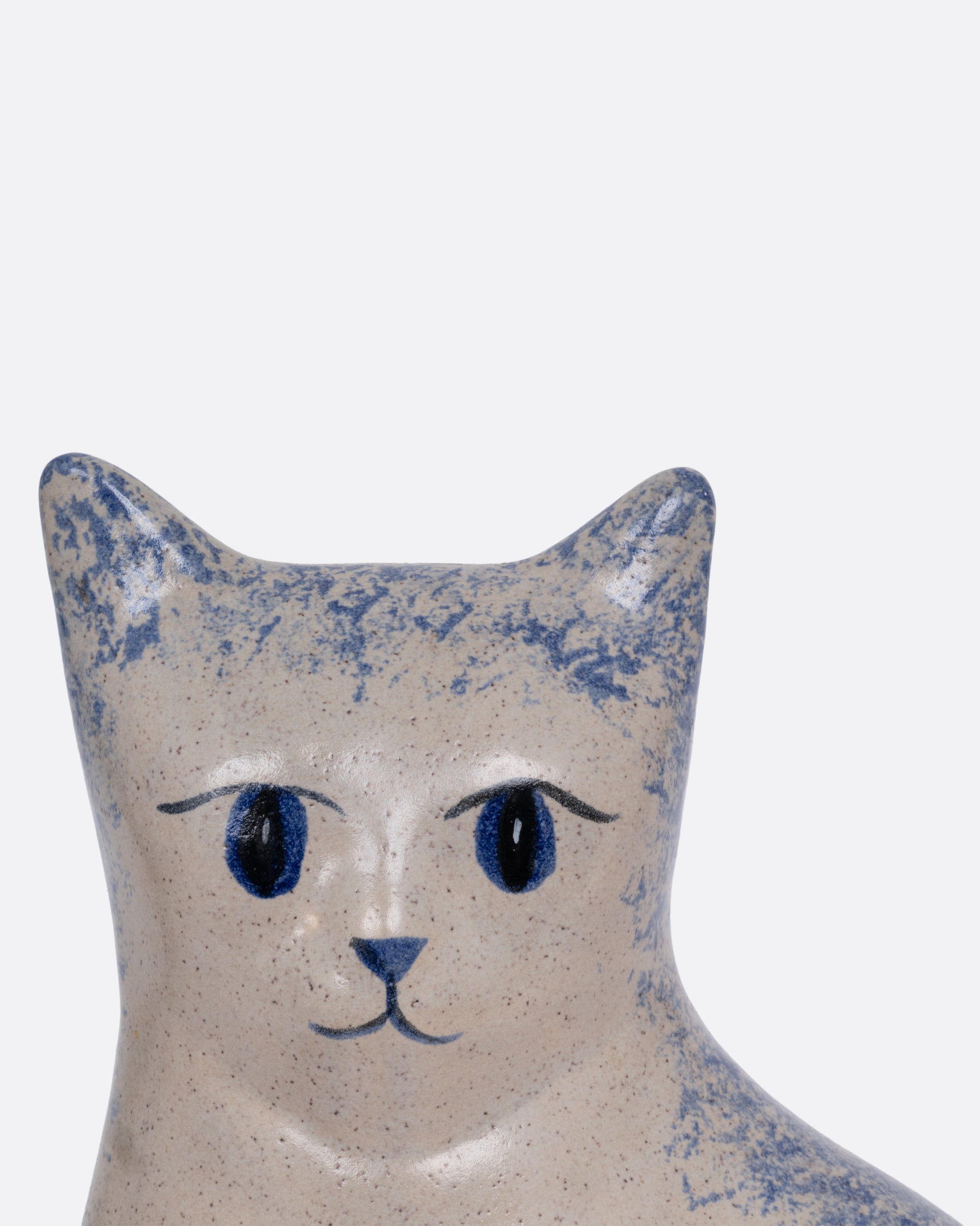 A close up of the face of a ceramic cat figurine with blue speckles, shown from the front.