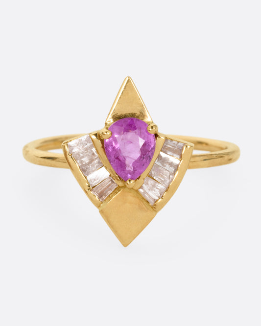 A yellow gold ring with a pink sapphire and baguette diamonds, shown from the front.