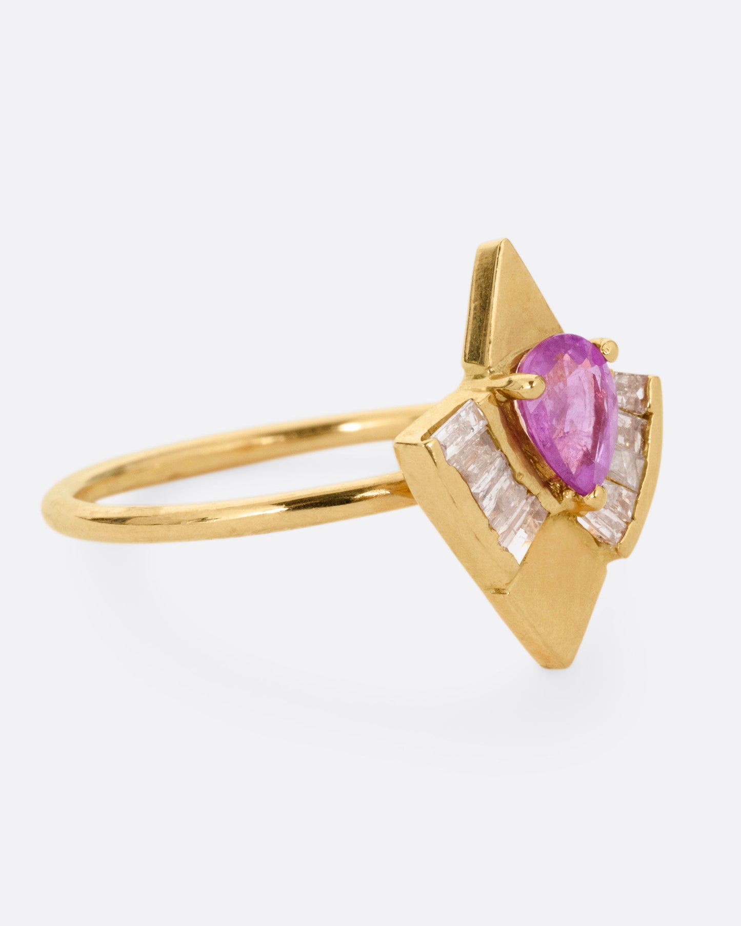 A yellow gold ring with a pink sapphire and baguette diamonds, shown from the side.
