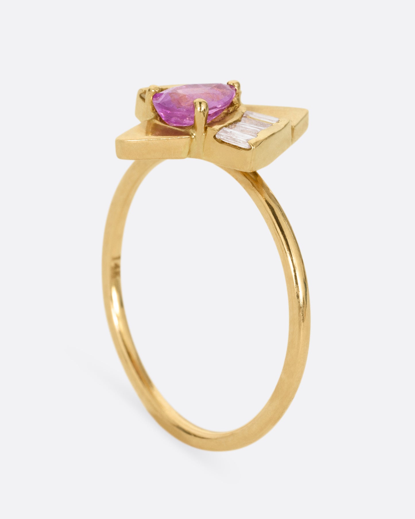 A yellow gold ring with a pink sapphire and baguette diamonds, shown from the side standing up.