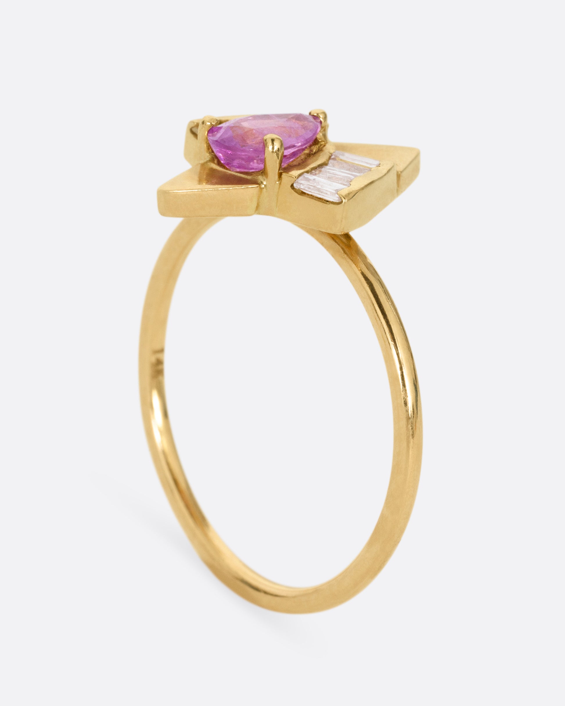 A yellow gold ring with a pink sapphire and baguette diamonds, shown from the side standing up.
