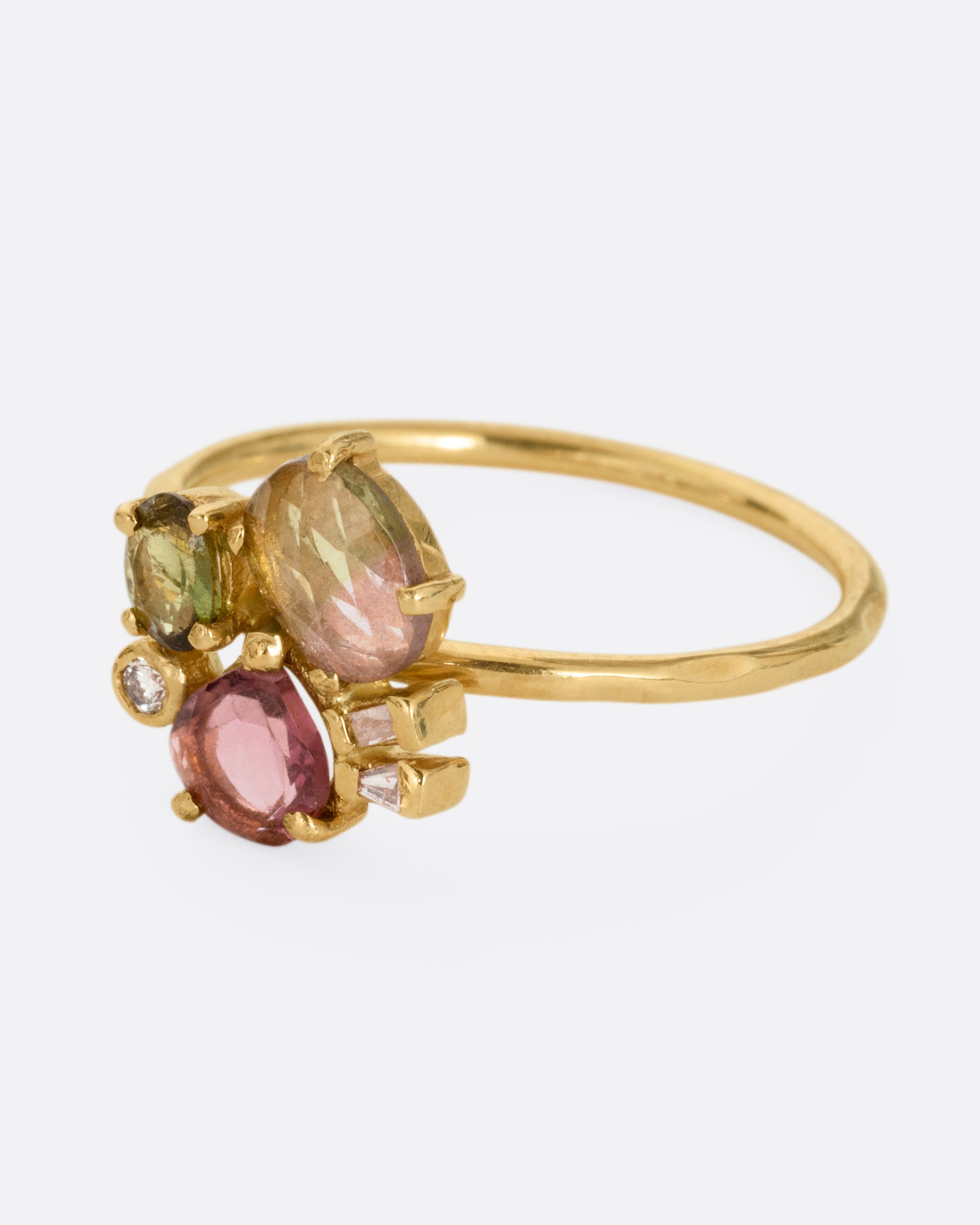 A yellow gold ring with green and pink tourmalines and three diamonds. Shown from the side.