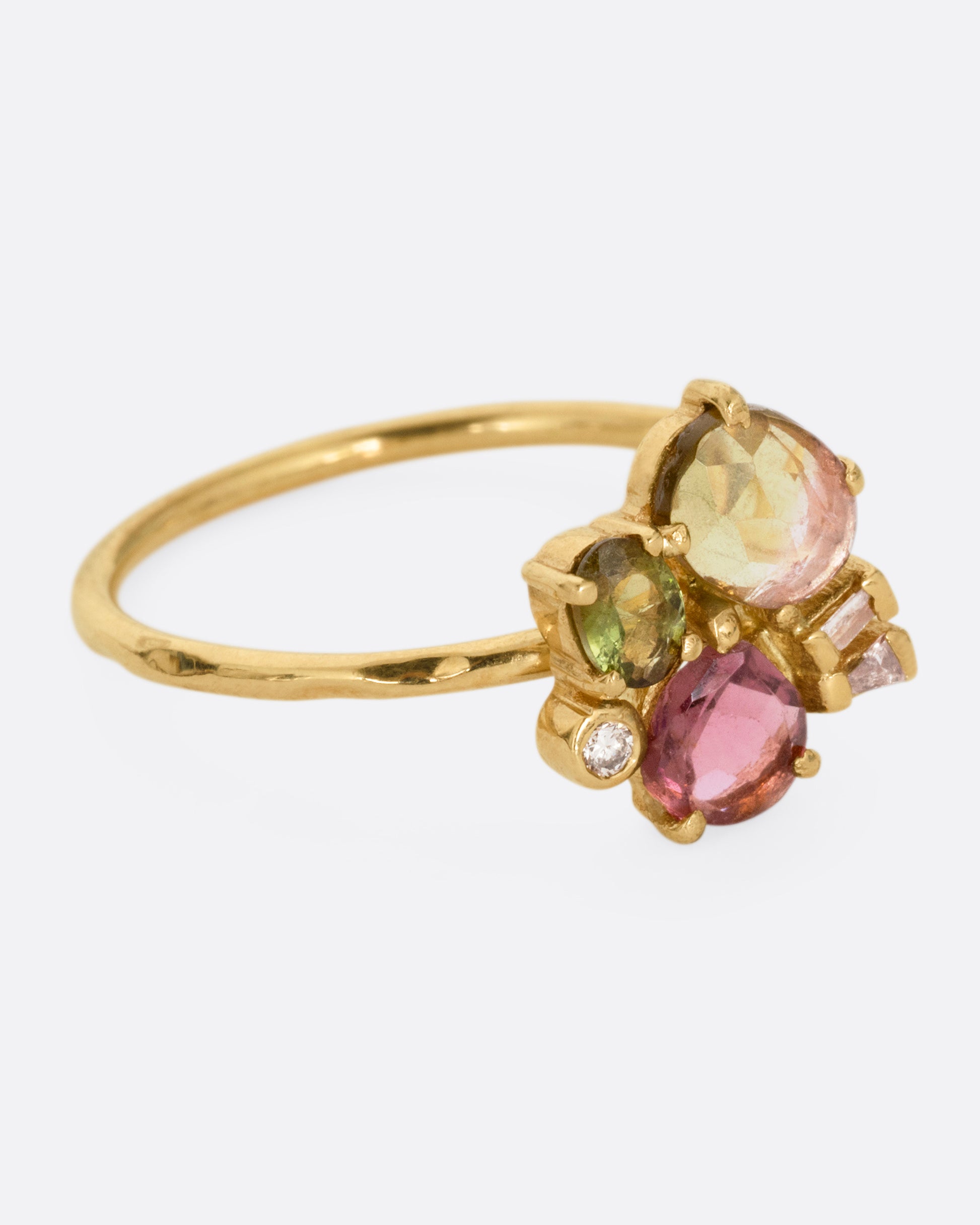 A yellow gold ring with green and pink tourmalines and three diamonds. Shown from the side.