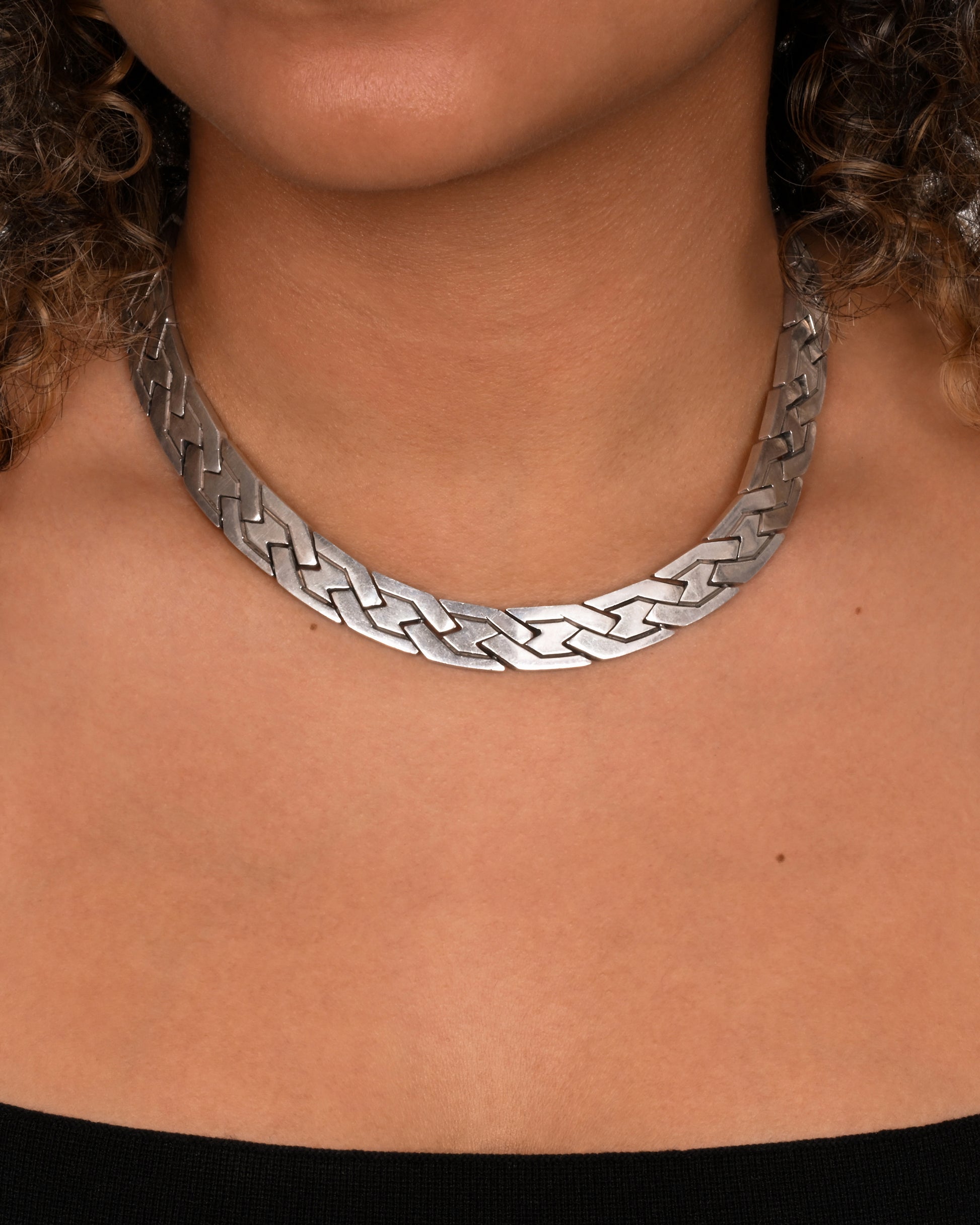 A flat woven link sterling silver necklace. Shown on a neck.