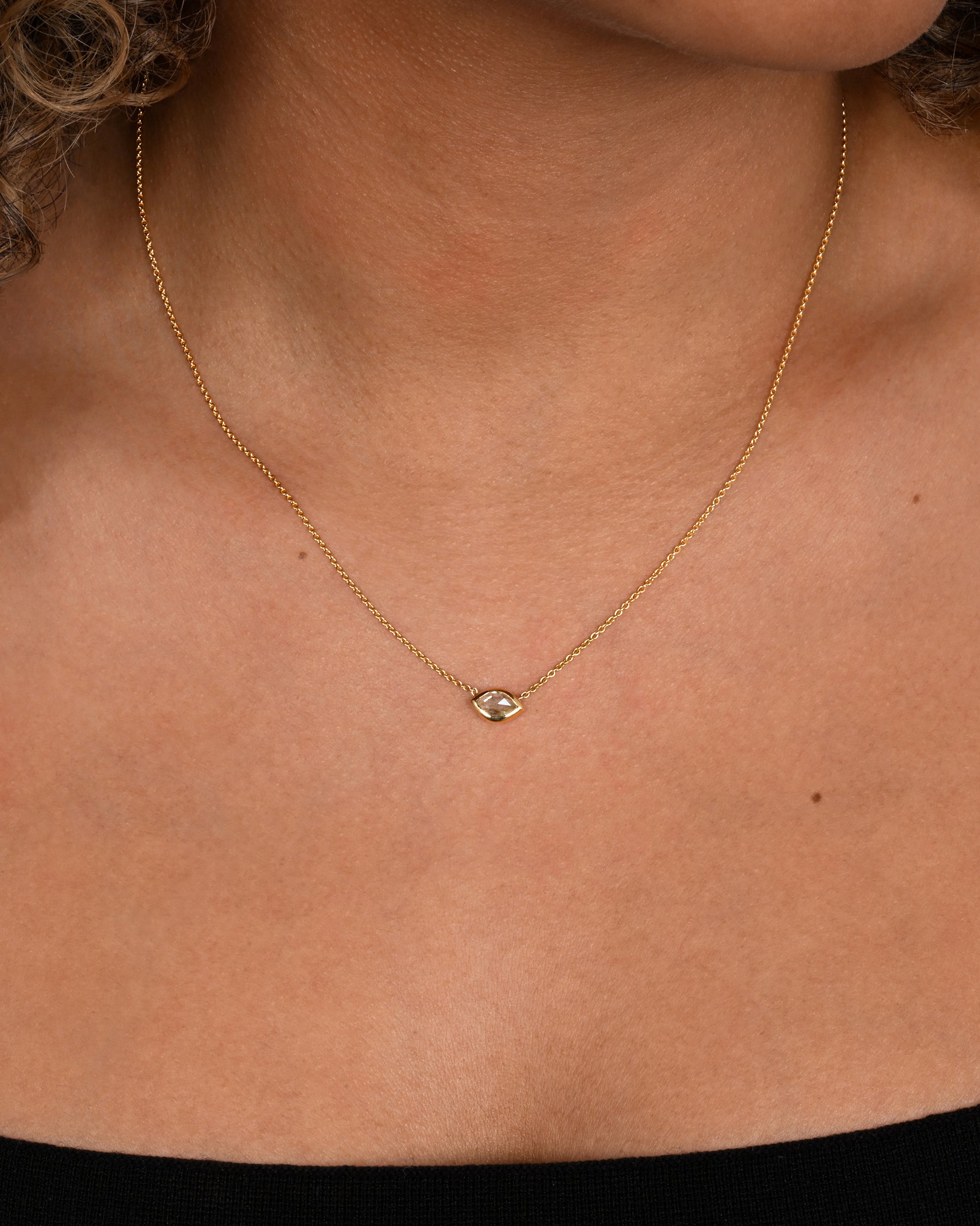 A yellow gold necklace with a  marquis shaped diamond. Shown on a neck.