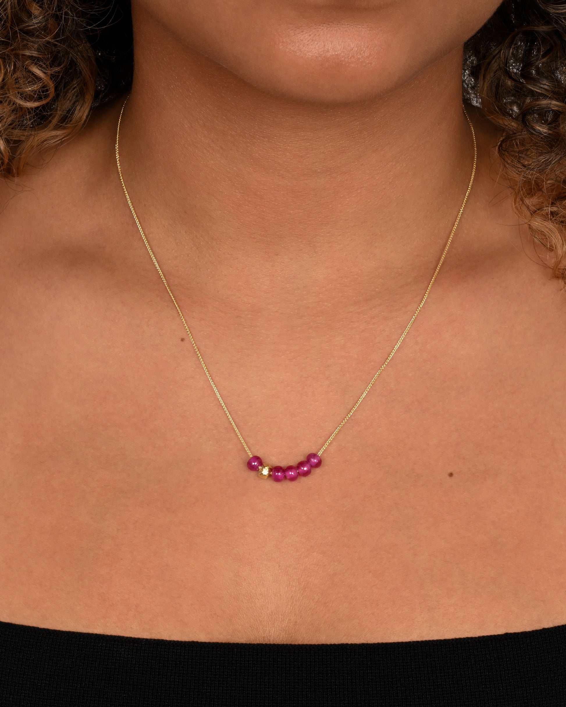 yellow gold necklace with pink sapphire pendant shown worn around the neck