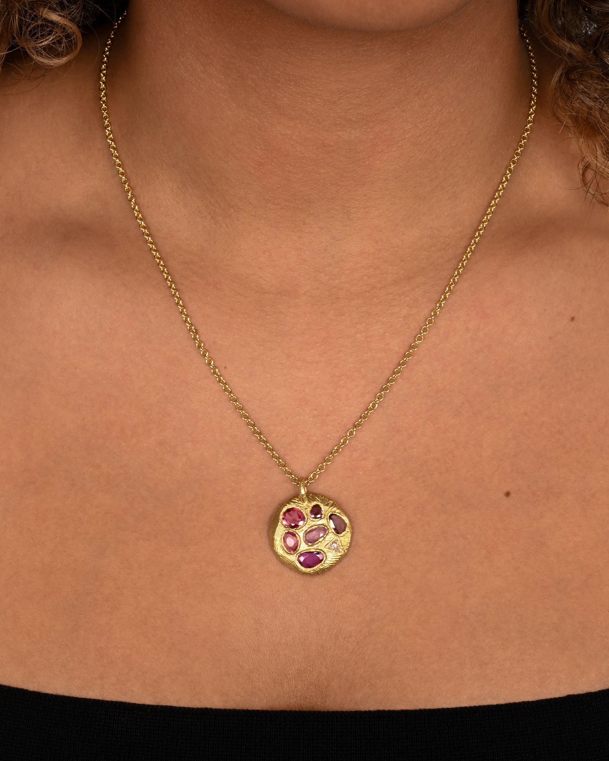 yellow gold necklace with pink sapphire pendant shown worn around the neck