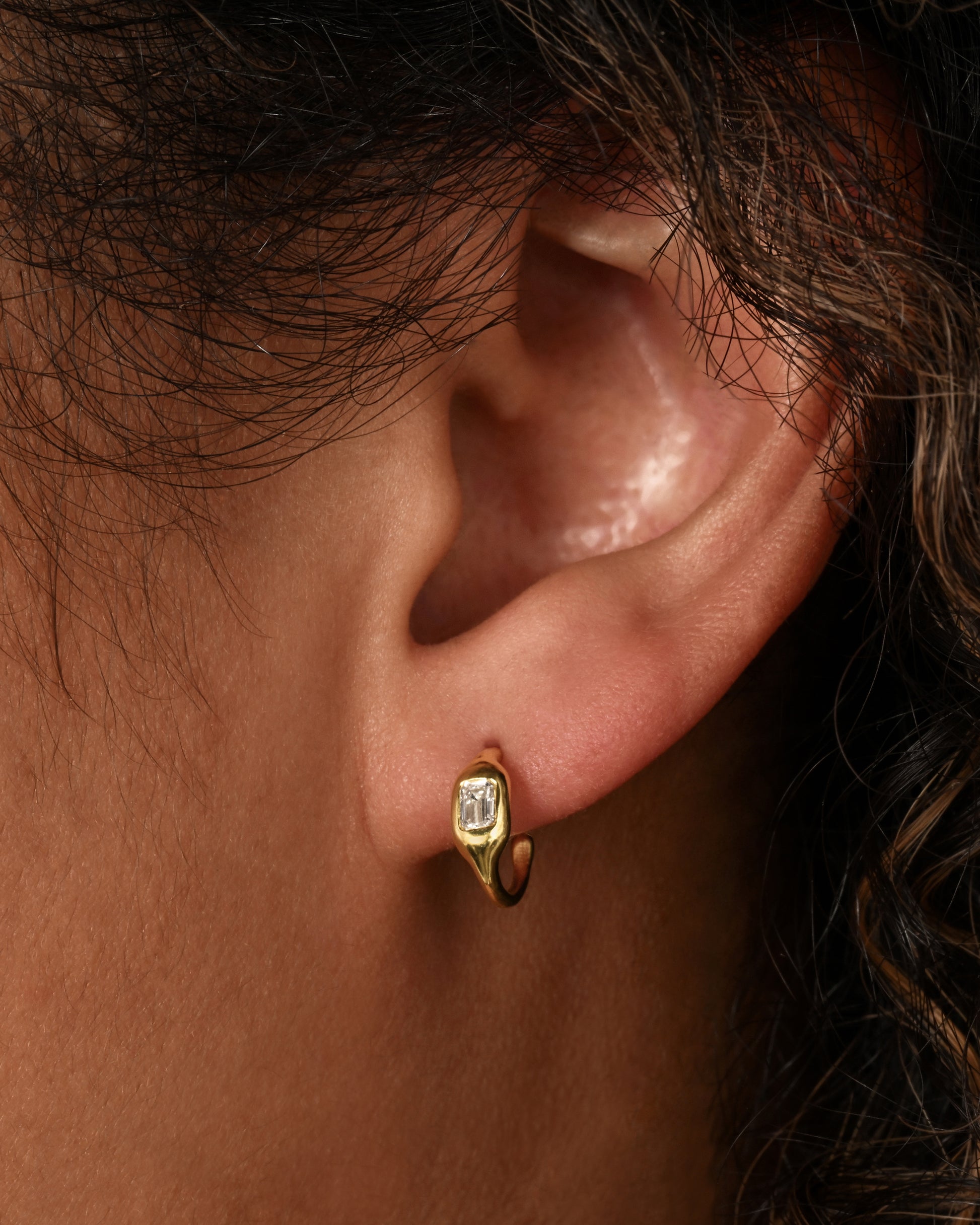 A yellow gold hoop with a single baguette diamond. Shown on an ear.