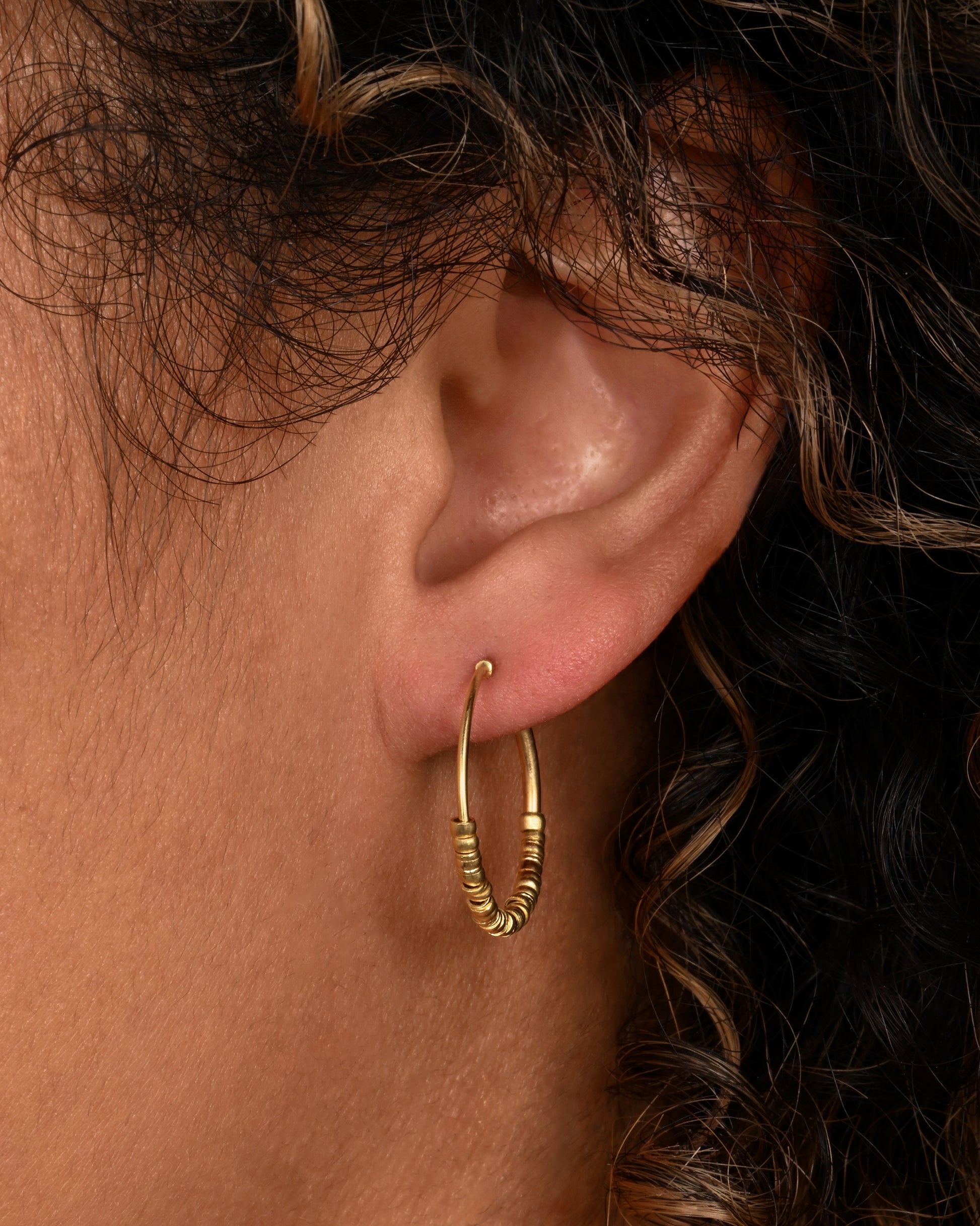 Yellow gold hoop earrings with beads and tube closure. Shown on an ear.