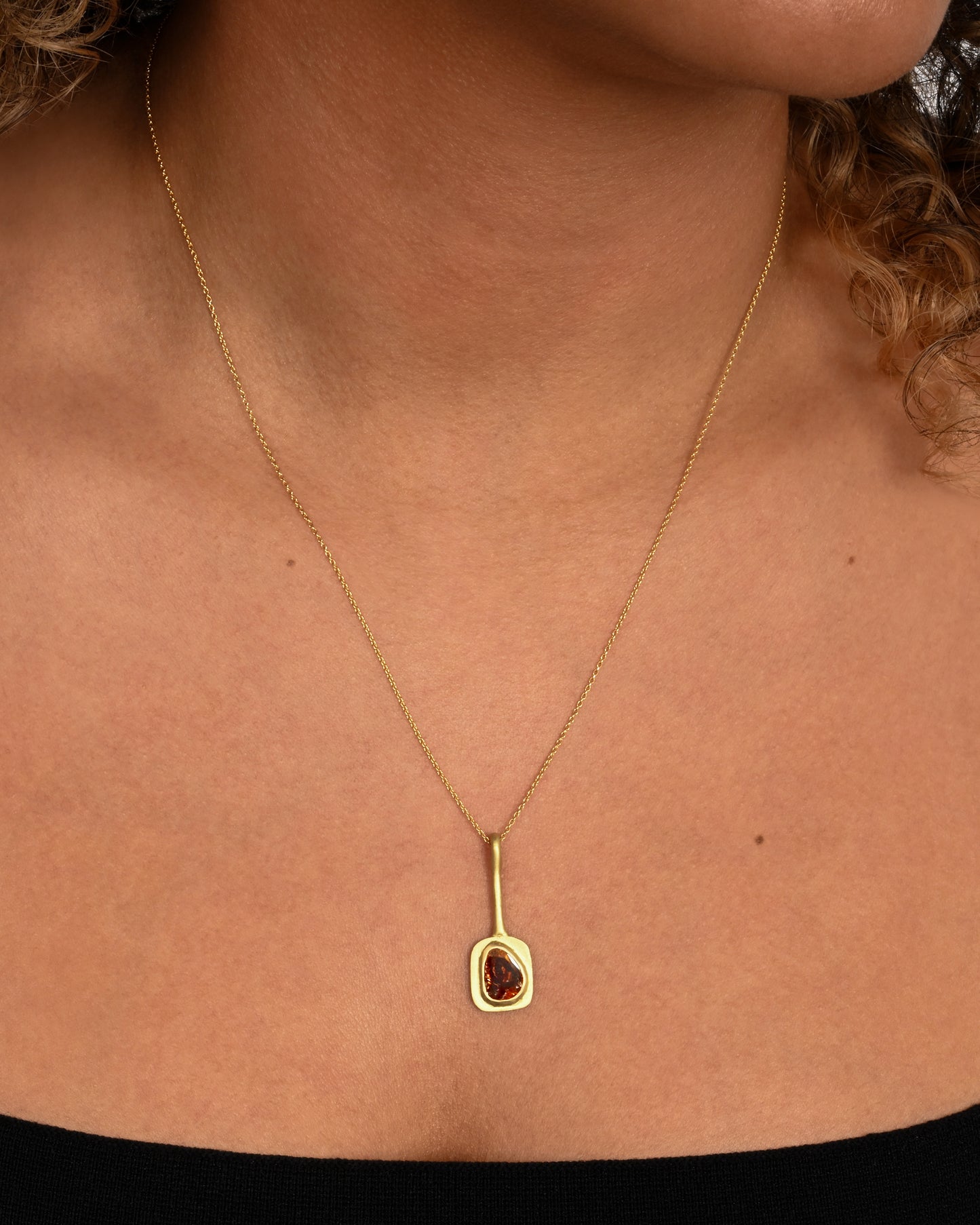 A yellow gold necklace with an ochre diamond pendant, shown worn around a neck.