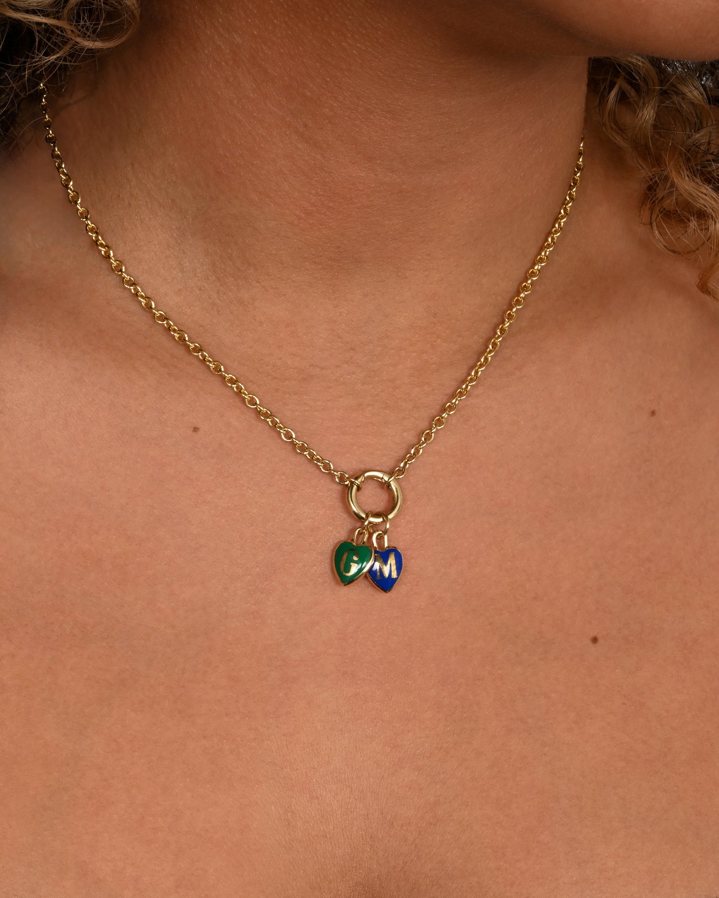 A yellow gold letter "T" heart shaped charm with black enamel. Shown worn styled with other heart charms on a chain with a charm holder.
