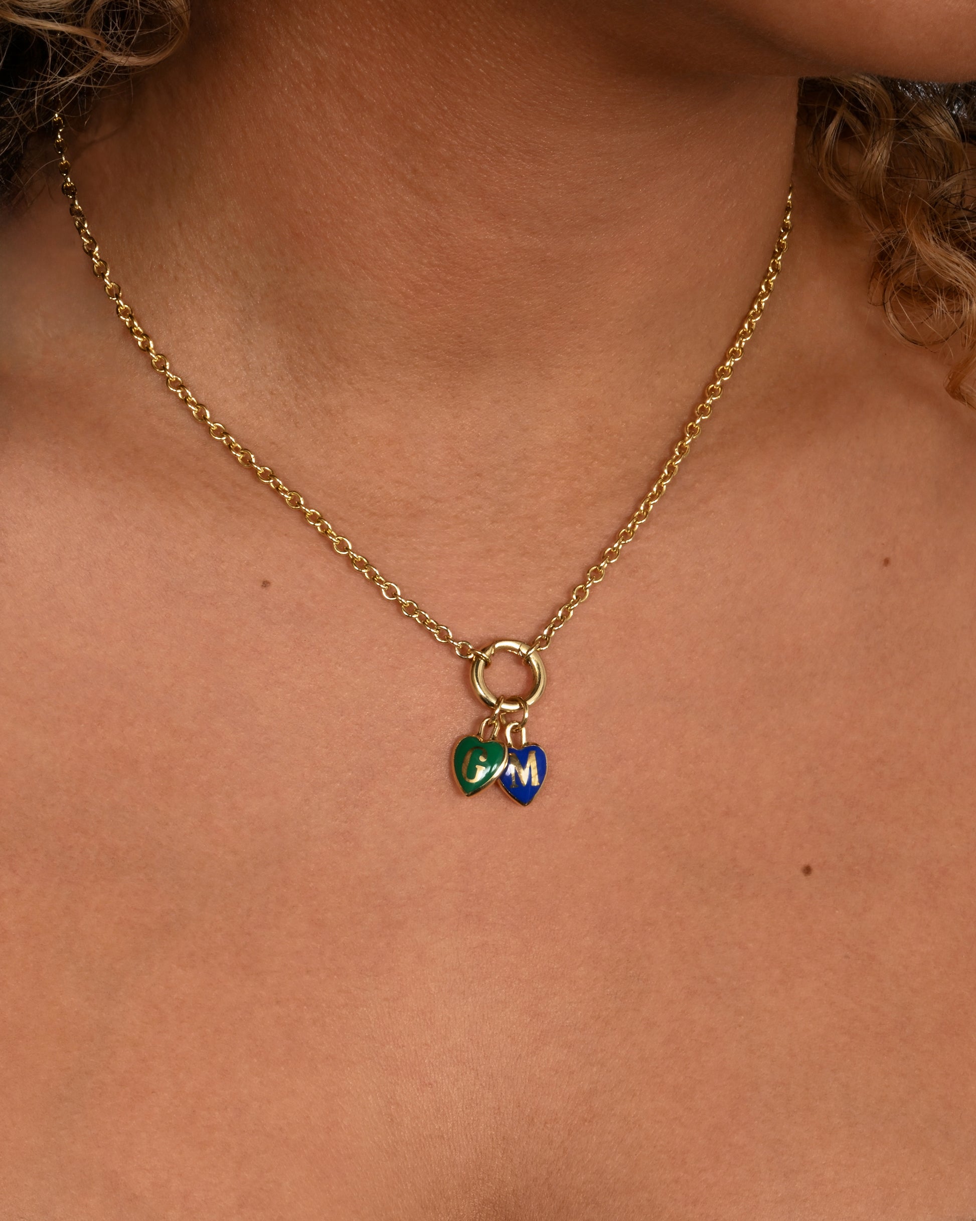 A yellow gold letter "T" heart shaped charm with black enamel. Shown worn styled with other heart charms on a chain with a charm holder.