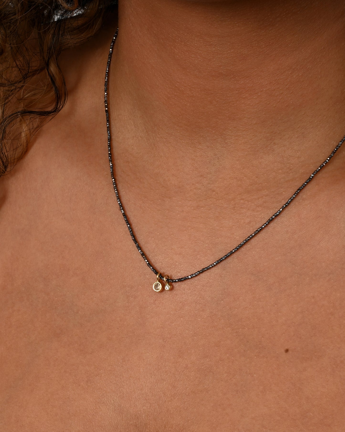 An oxidized silver beaded necklace with two diamond charms. Shown on a neck.