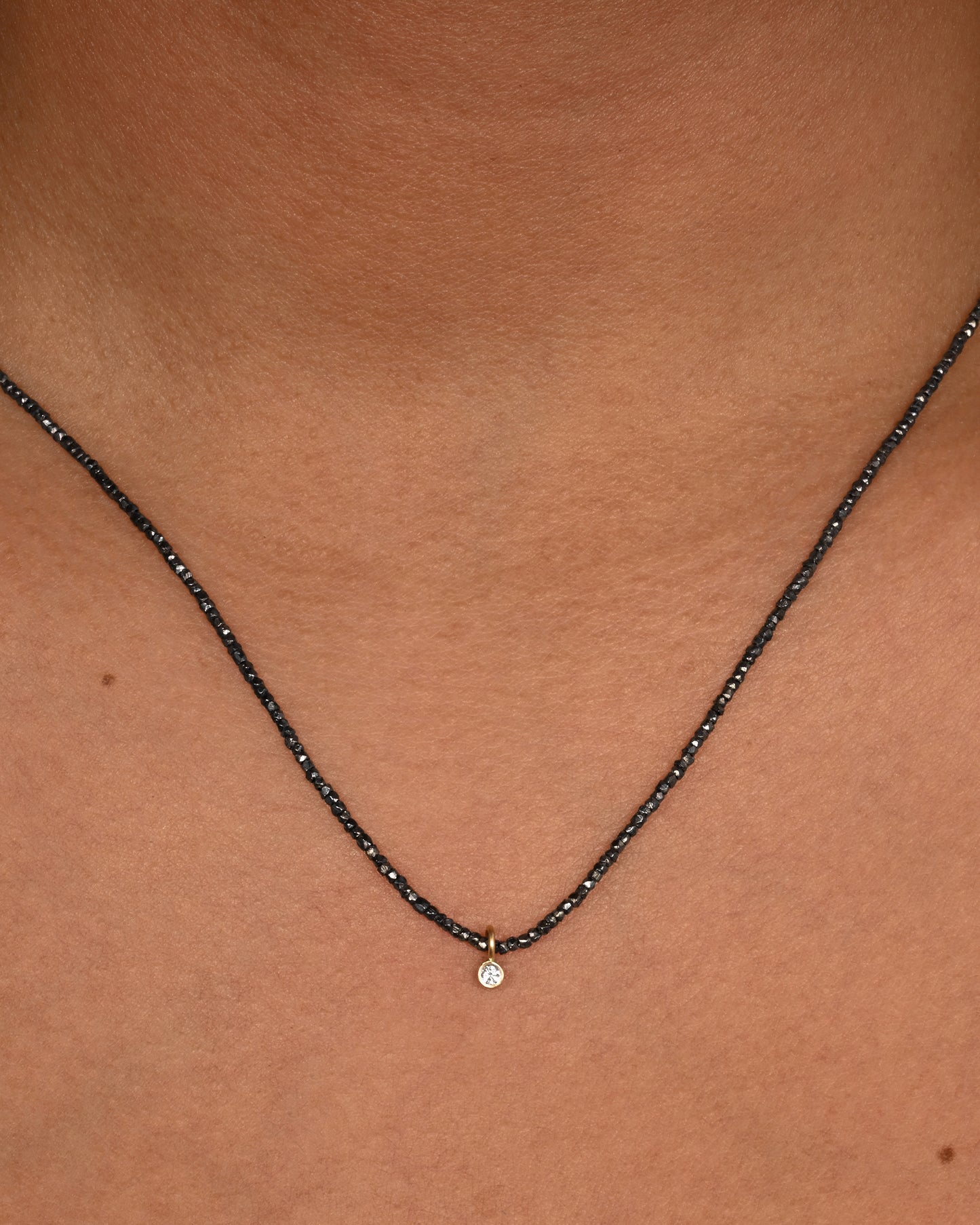 An oxidized silver necklace with a single diamond pendant. Shown on a neck.