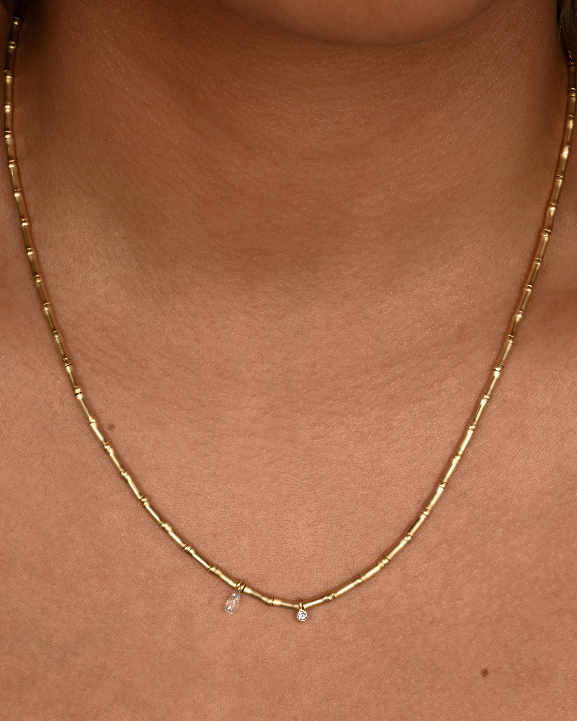 A yellow gold tube beaded necklace with two diamonds. Shown on a neck.