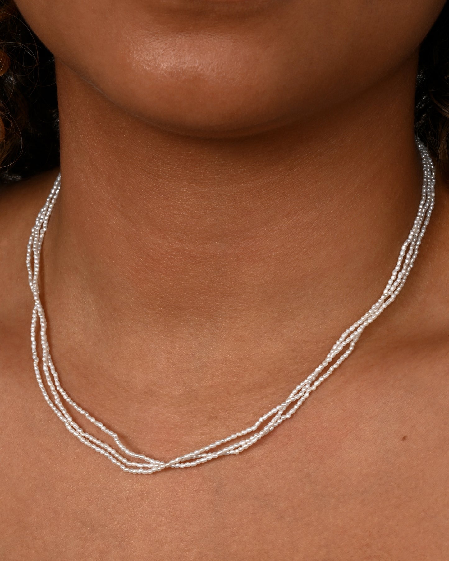 A three strand pearl necklace, shown on a neck.