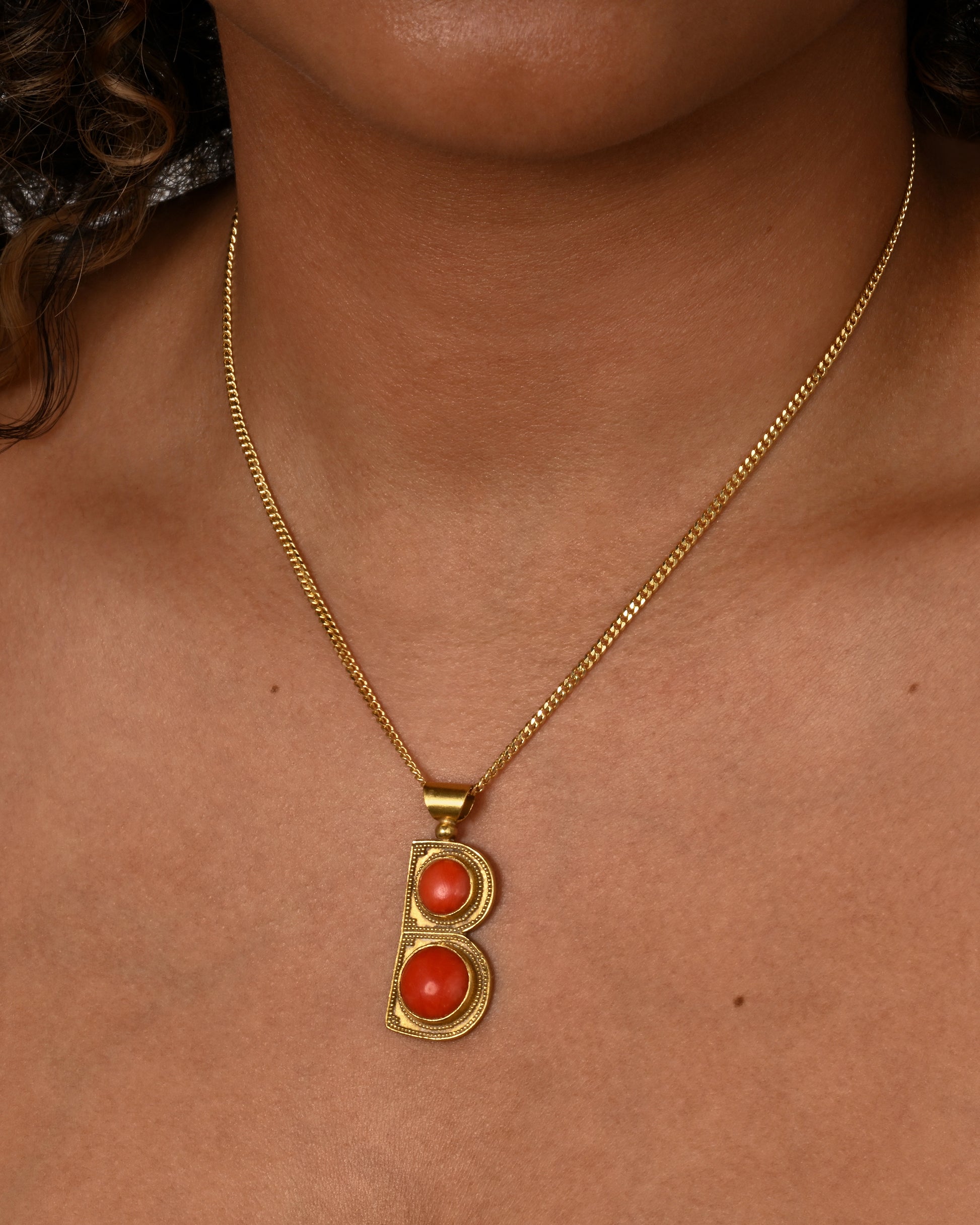 A yellow gold letter "B" pendant with coral circles. Shown worn on a chain.