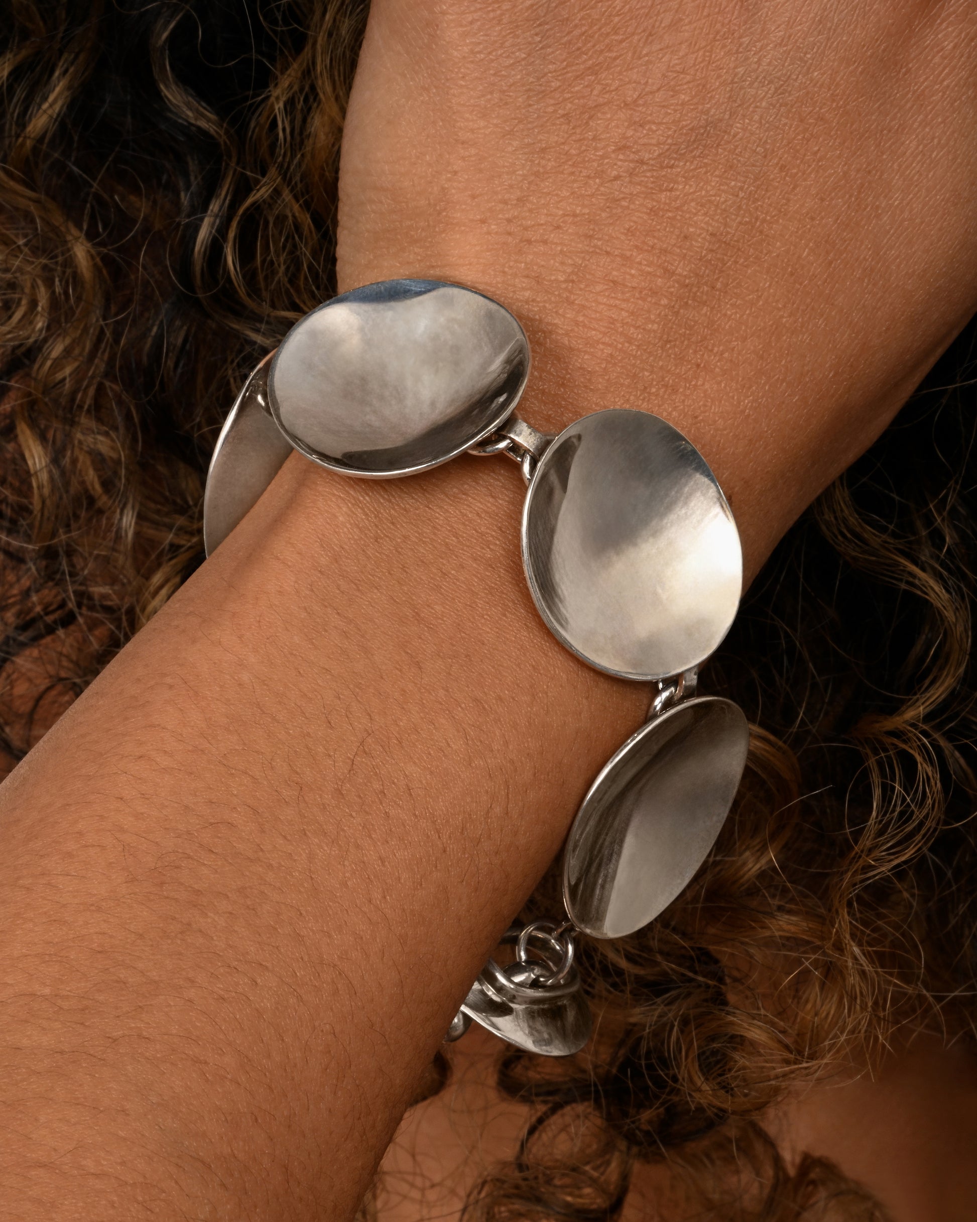 A sterling silver bracelet with concave circle links and a toggle closure. Shown on a wrist.