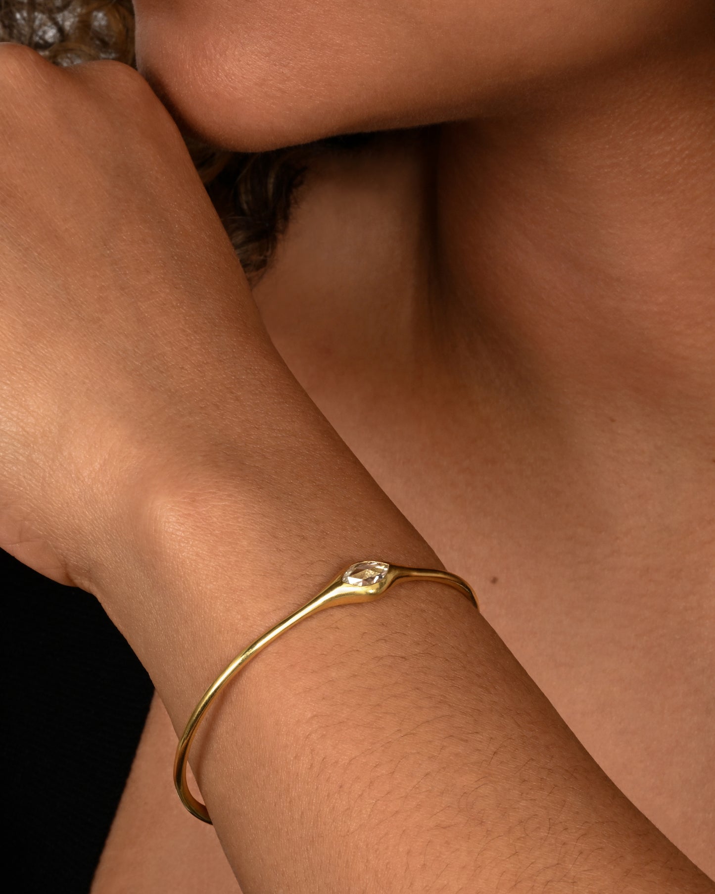 A yellow gold cuff with a marquis diamond. Shown on an arm.