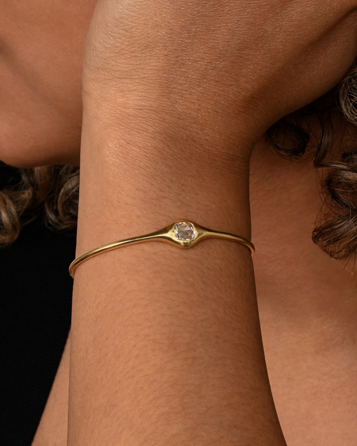 A yellow gold cuff bracelet with a rose cut cushion shaped diamond. Shown on a wrist.