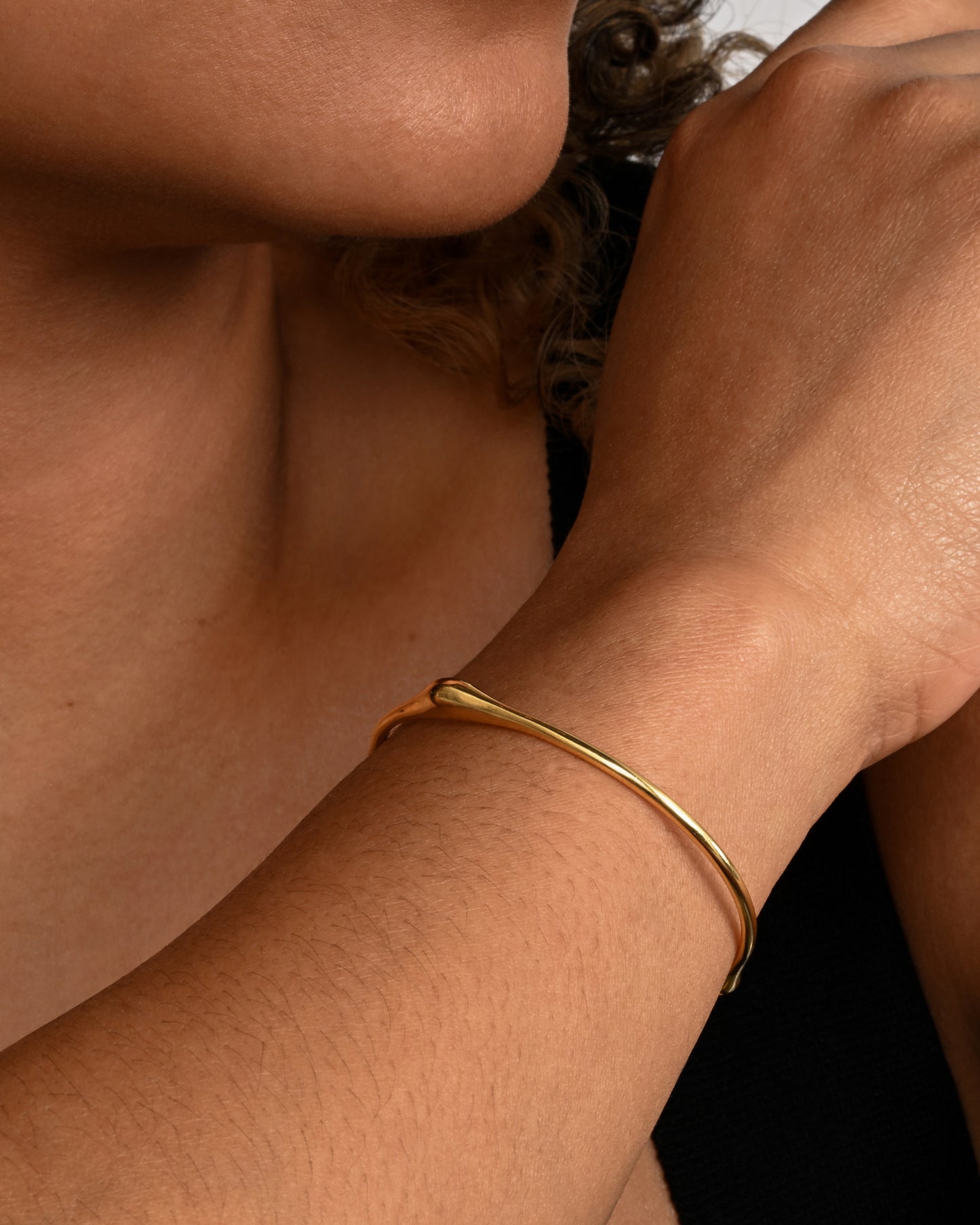 A yellow gold cuff bracelet with a bump. Shown on a wrist.