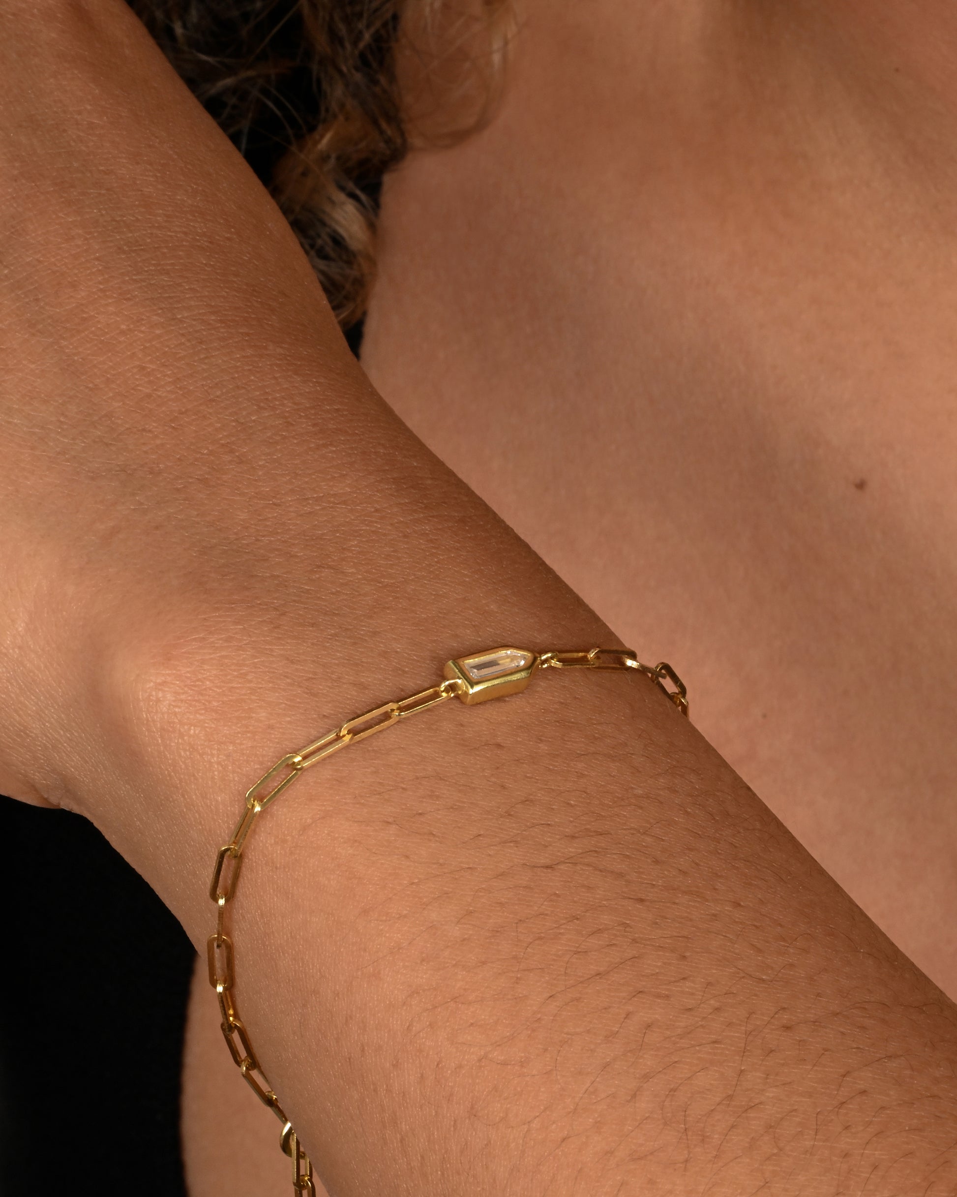 A yellow gold paperclip chain bracelet with a bullet shaped diamond channel. Shown on a wrist.