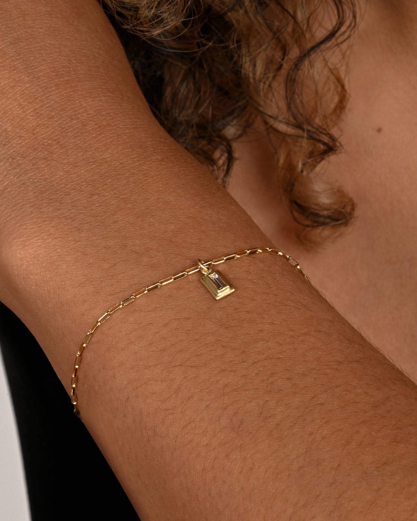 A yellow gold elongated rolo chain bracelet with a baguette diamond. Shown worn on a wrist.