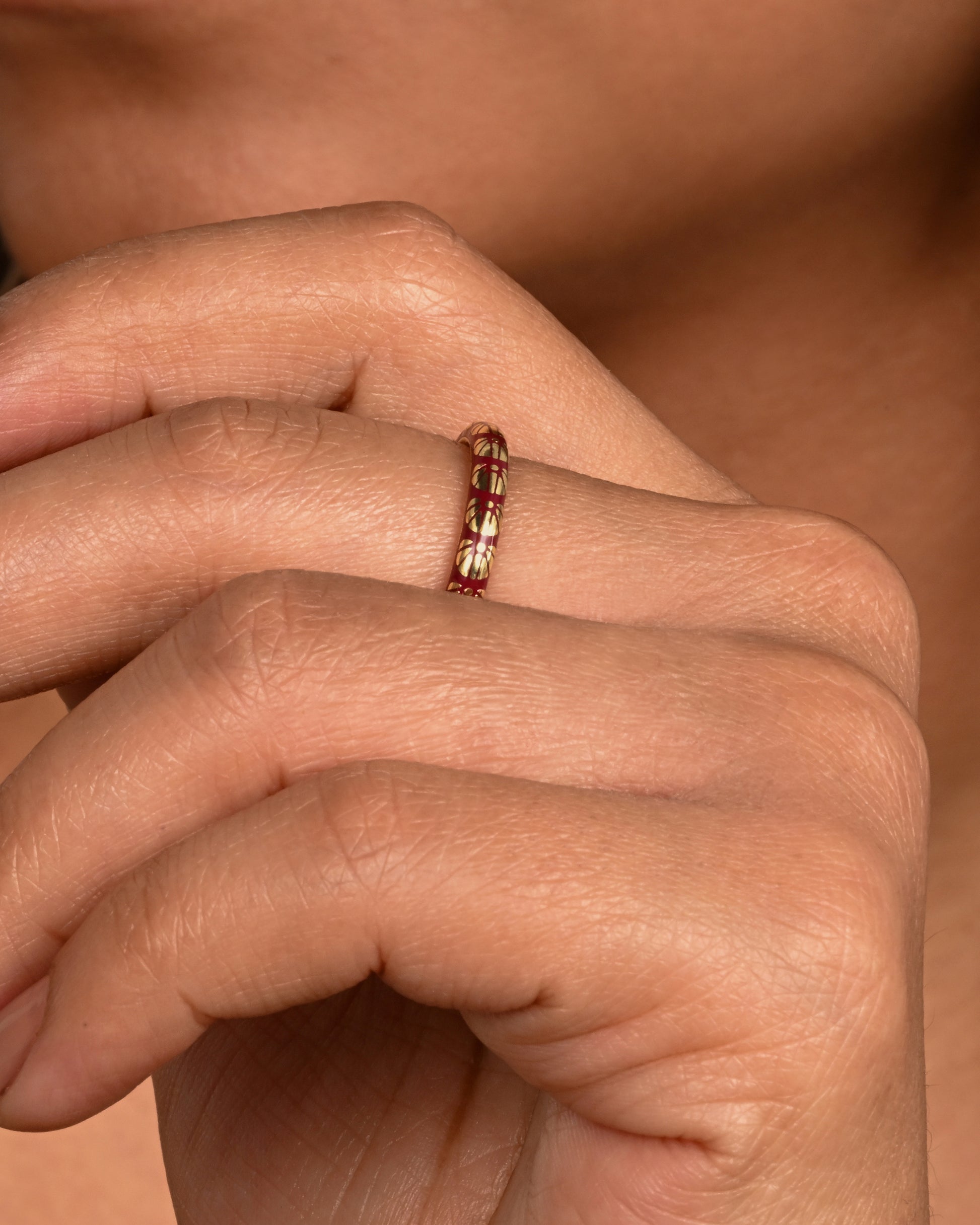 A yellow gold ring with burgundy enamel and a floral motif around the entire band. Shown worn.