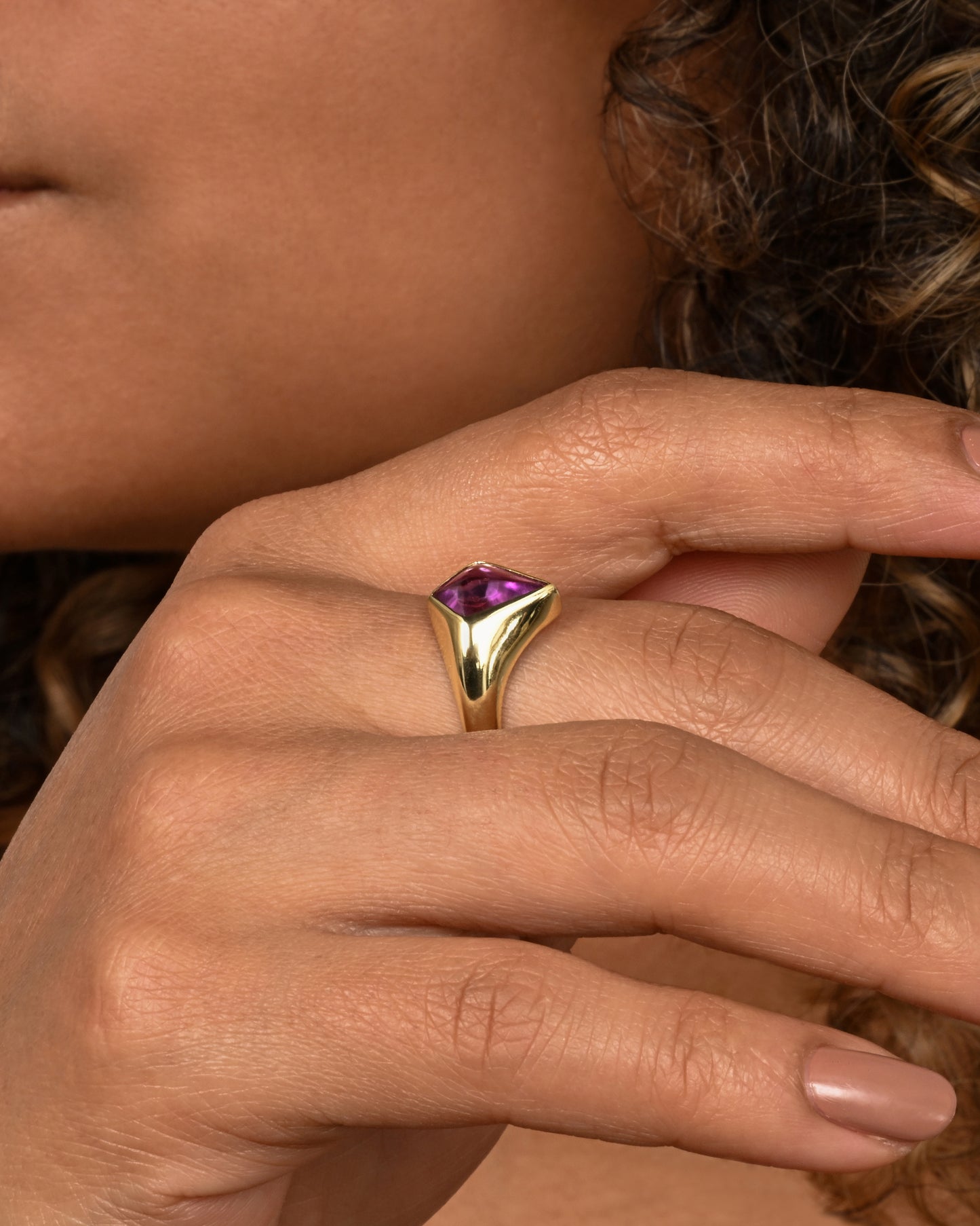 A yellow gold ring with a cabochon maroon kite shaped sapphire. Shown on a hand.