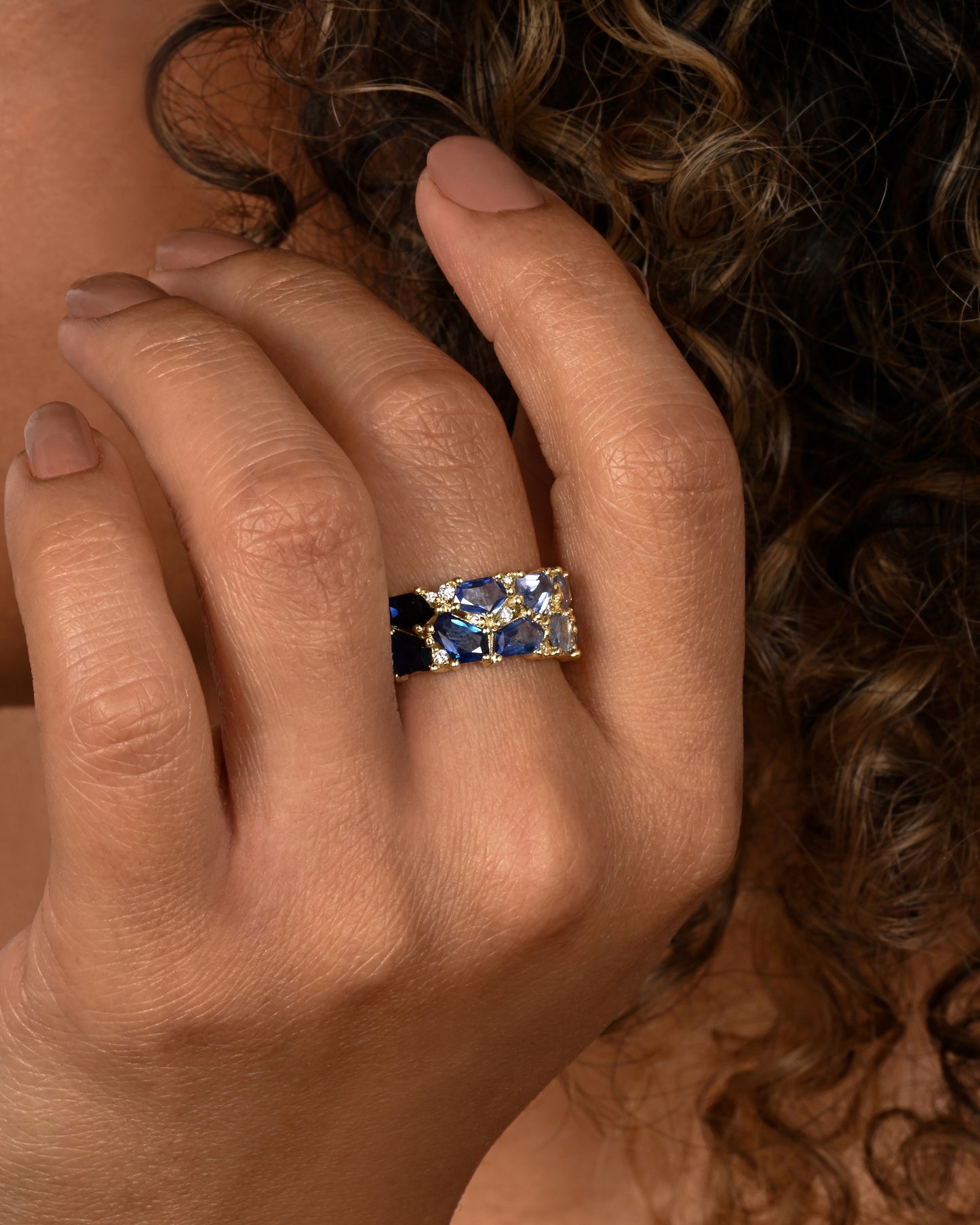 A yellow gold band with mosaic ombre blue sapphires and diamonds. Shown on a hand.