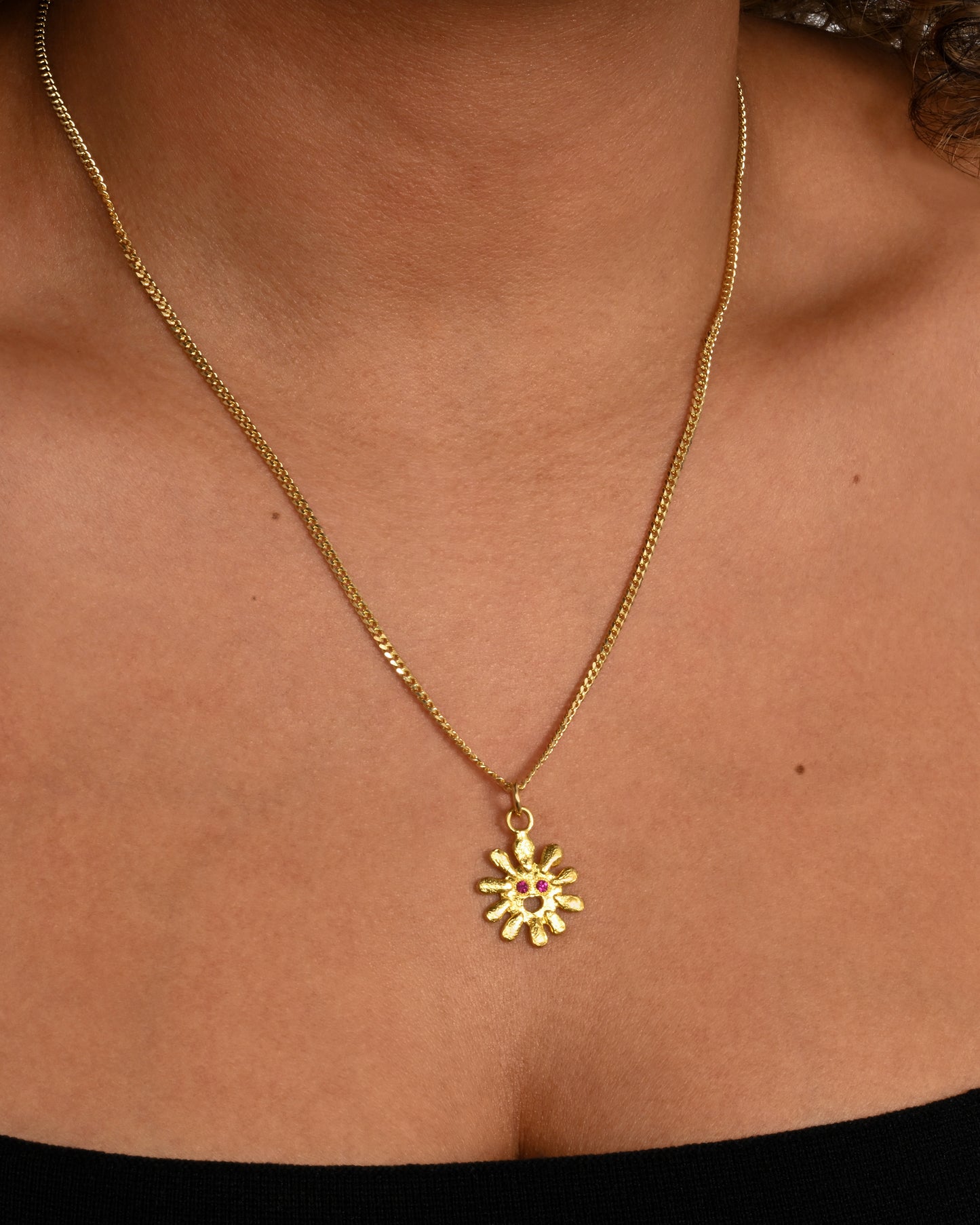 yellow gold sun pendant with ruby eyes shown on a chain around the neck