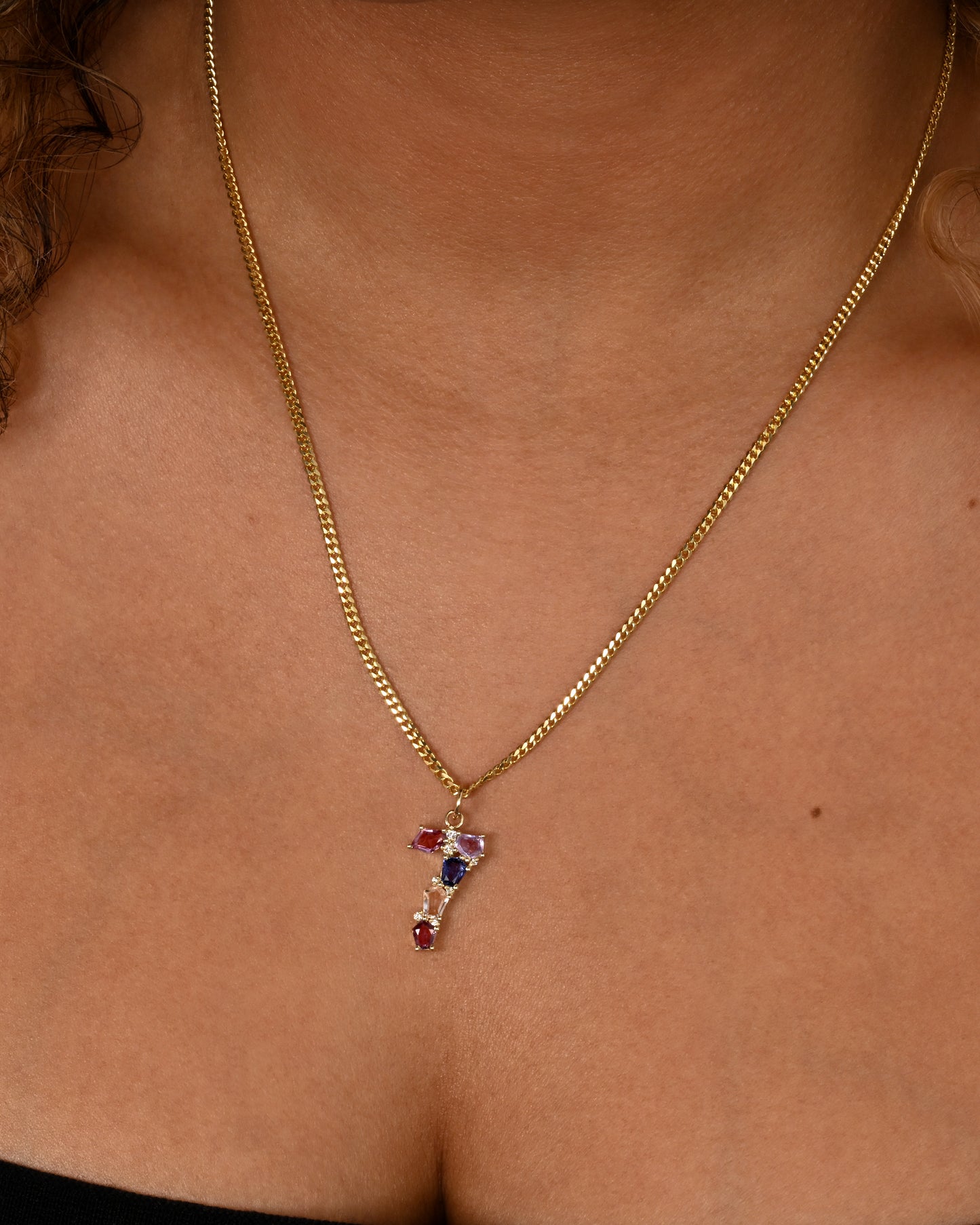 A yellow gold number "7" pendant made of mosaic multicolor sapphires and diamonds. Shown worn on a chain.