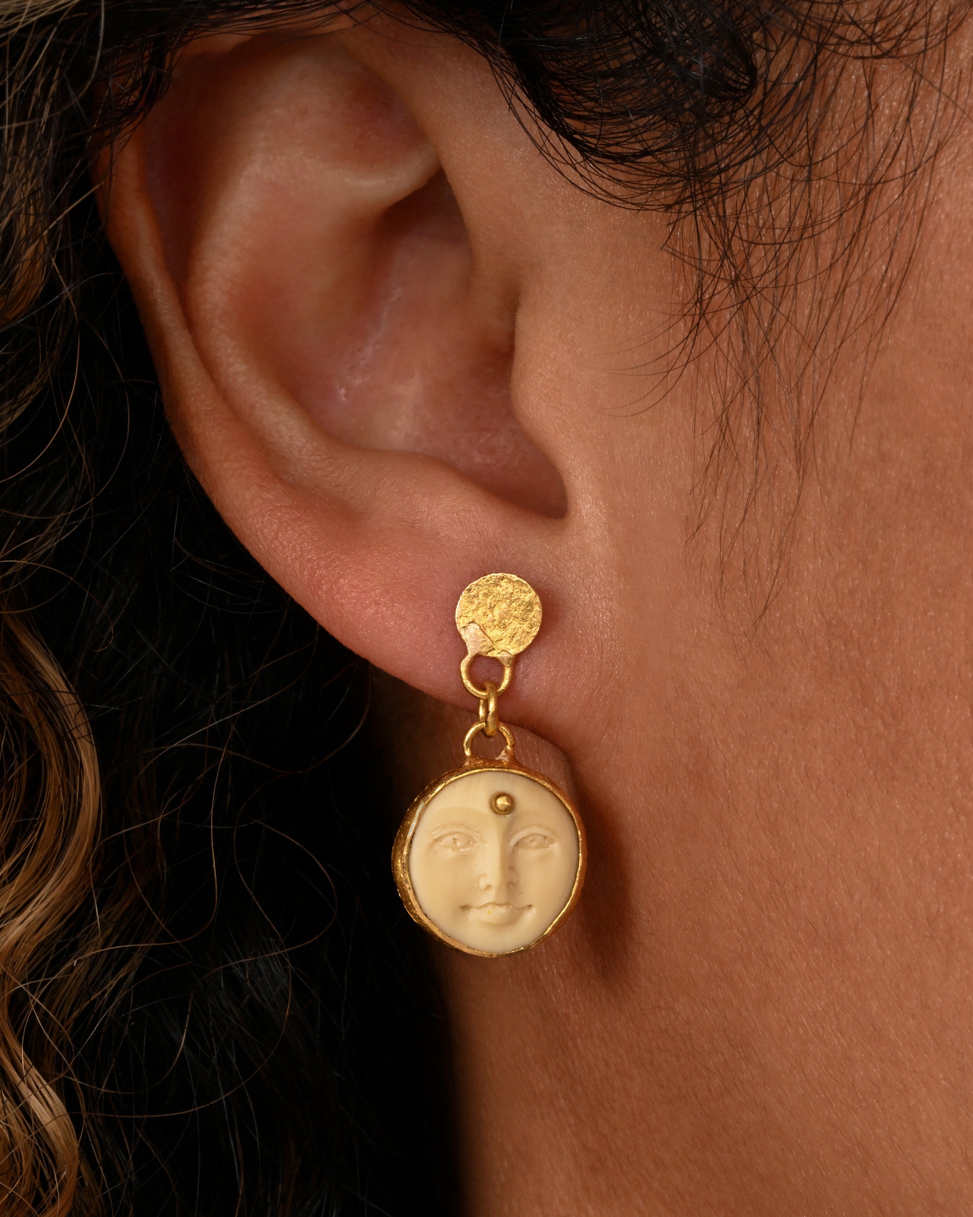 yellow gold carved bone moon face earrings shown on an ear