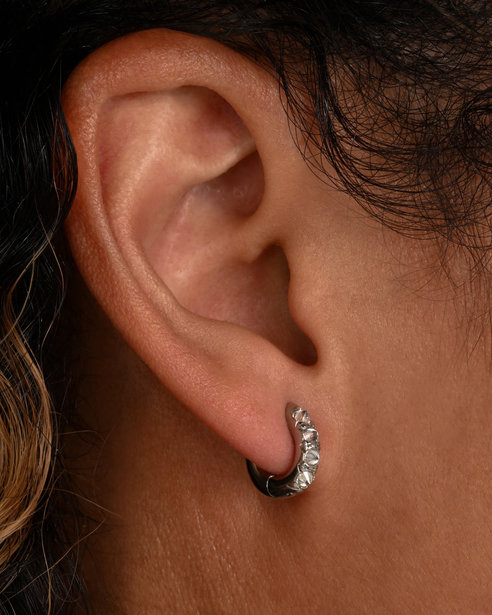 Inverted white diamonds set in platinum huggie hoops. Shown on an ear.