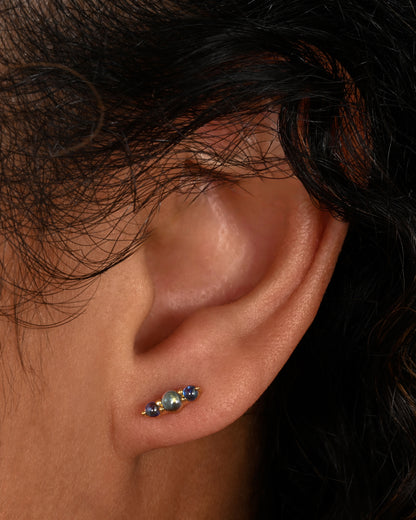 Stud earrings made of three blue sapphire cabochons set in yellow gold. Shown on an ear.