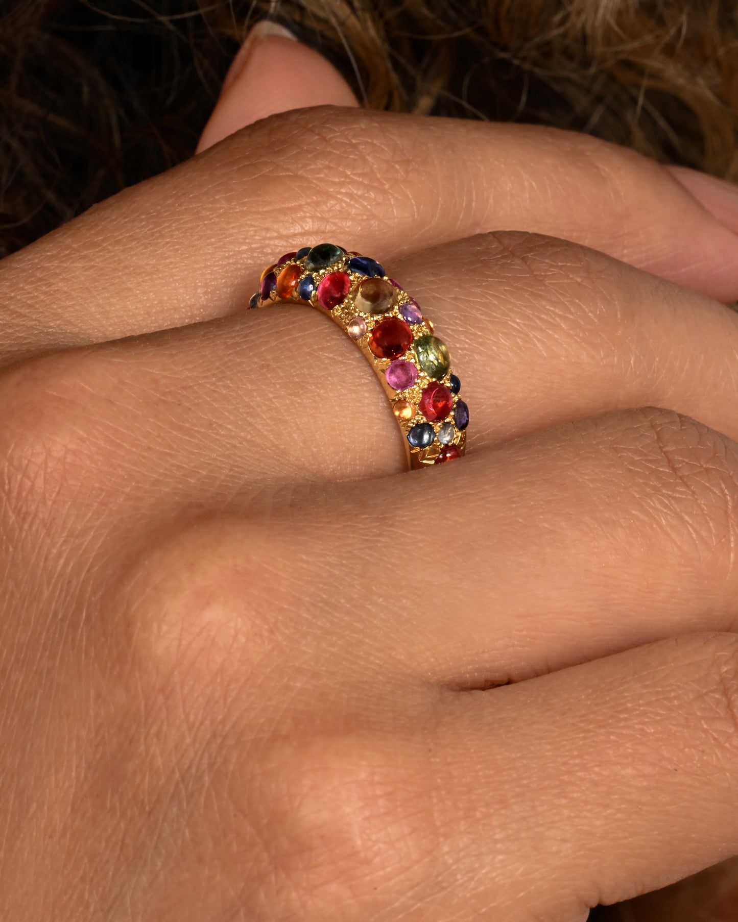 Multicolor sapphire cabochons set in an 18k yellow gold band. Shown on a hand.