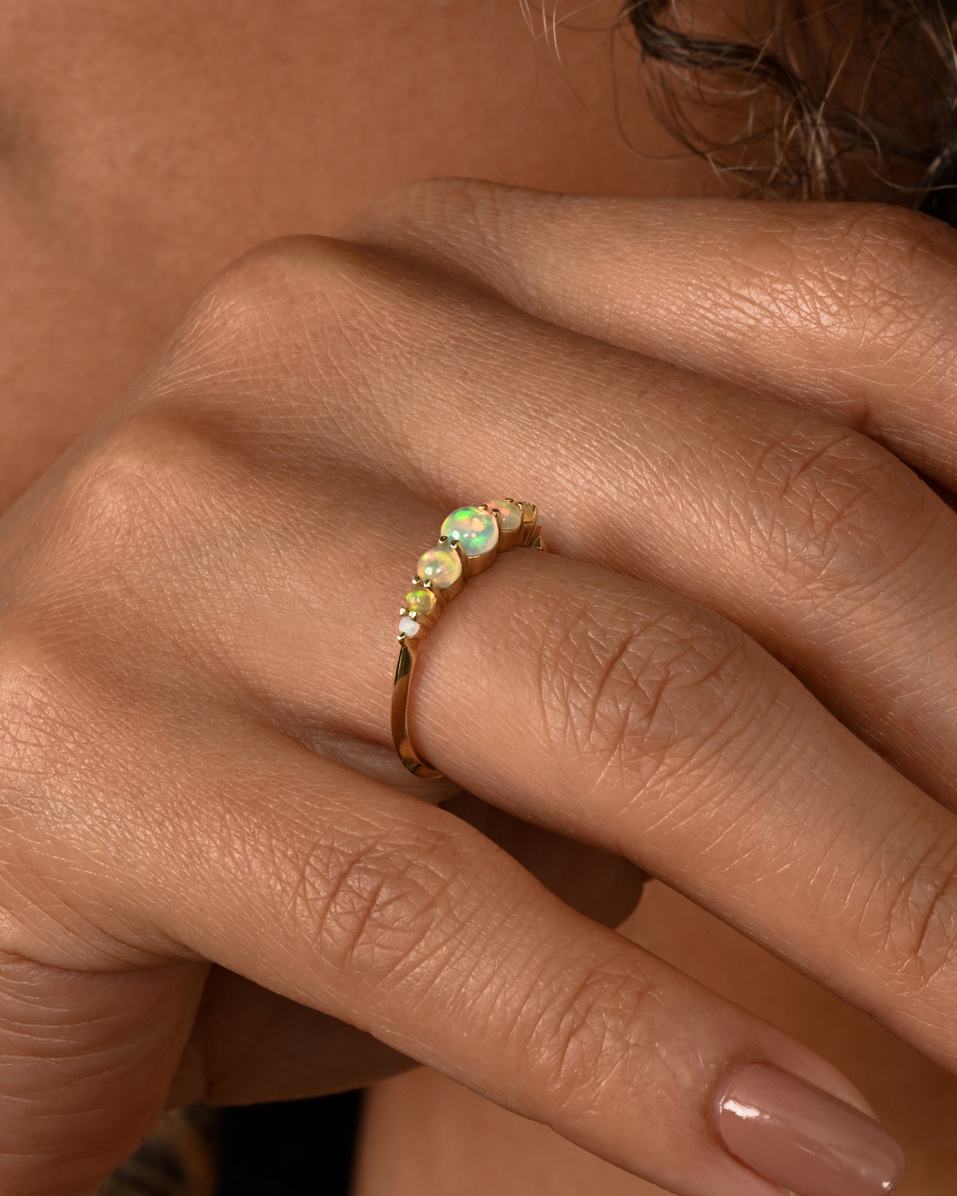 Seven graduated opals set in 18k yellow gold band. Shown on a hand.