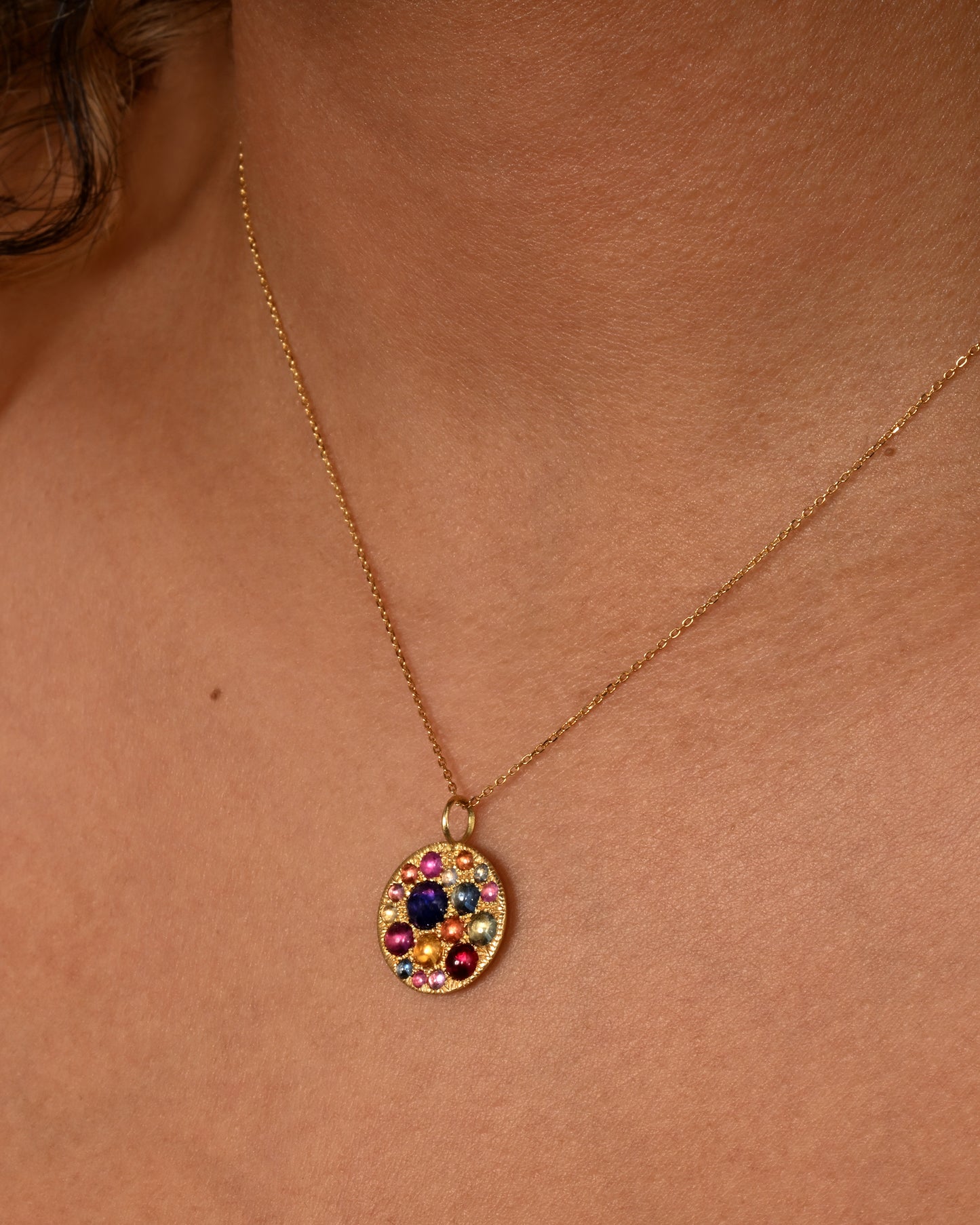 A yellow gold pendant with multicolor cabochon sapphires. Show worn on a chain.