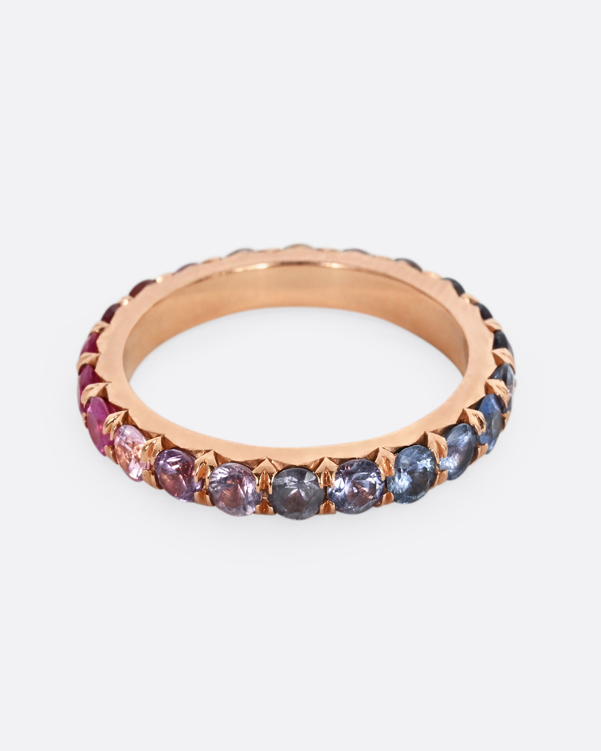 A rose gold eternity band with pink and blue cut sapphires.