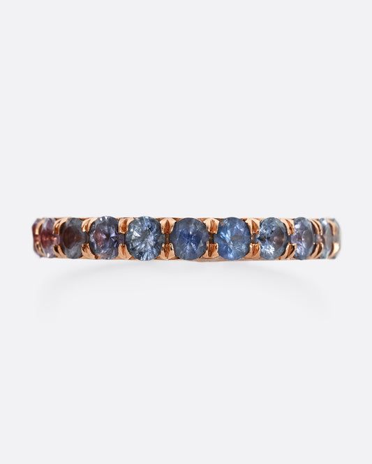 A rose gold eternity band with pink and blue cut sapphires. 