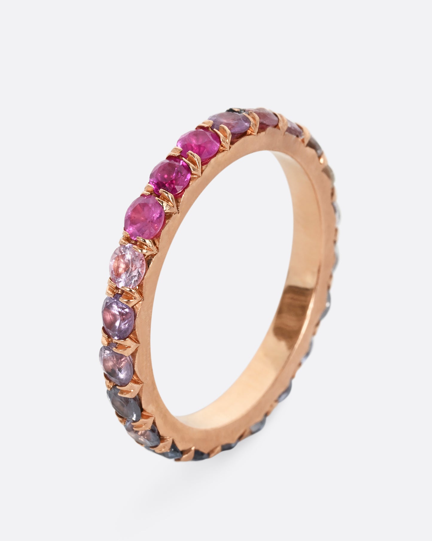 A rose gold eternity band with pink and blue cut sapphires. Shown from the side, standing up.