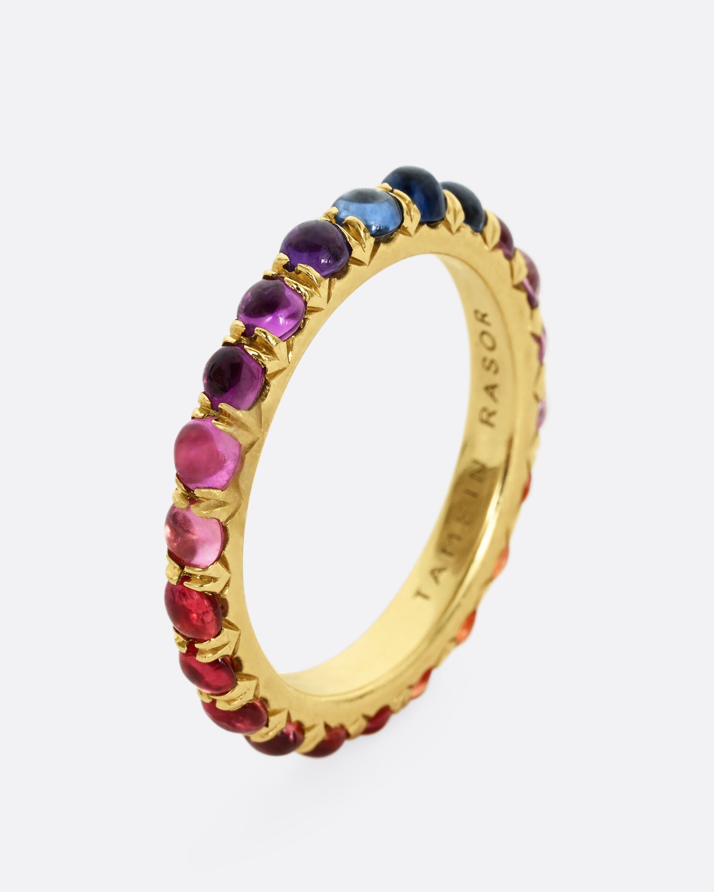 A yellow gold eternity band with rainbow sapphire cabochons. Shown from the side, standing up.