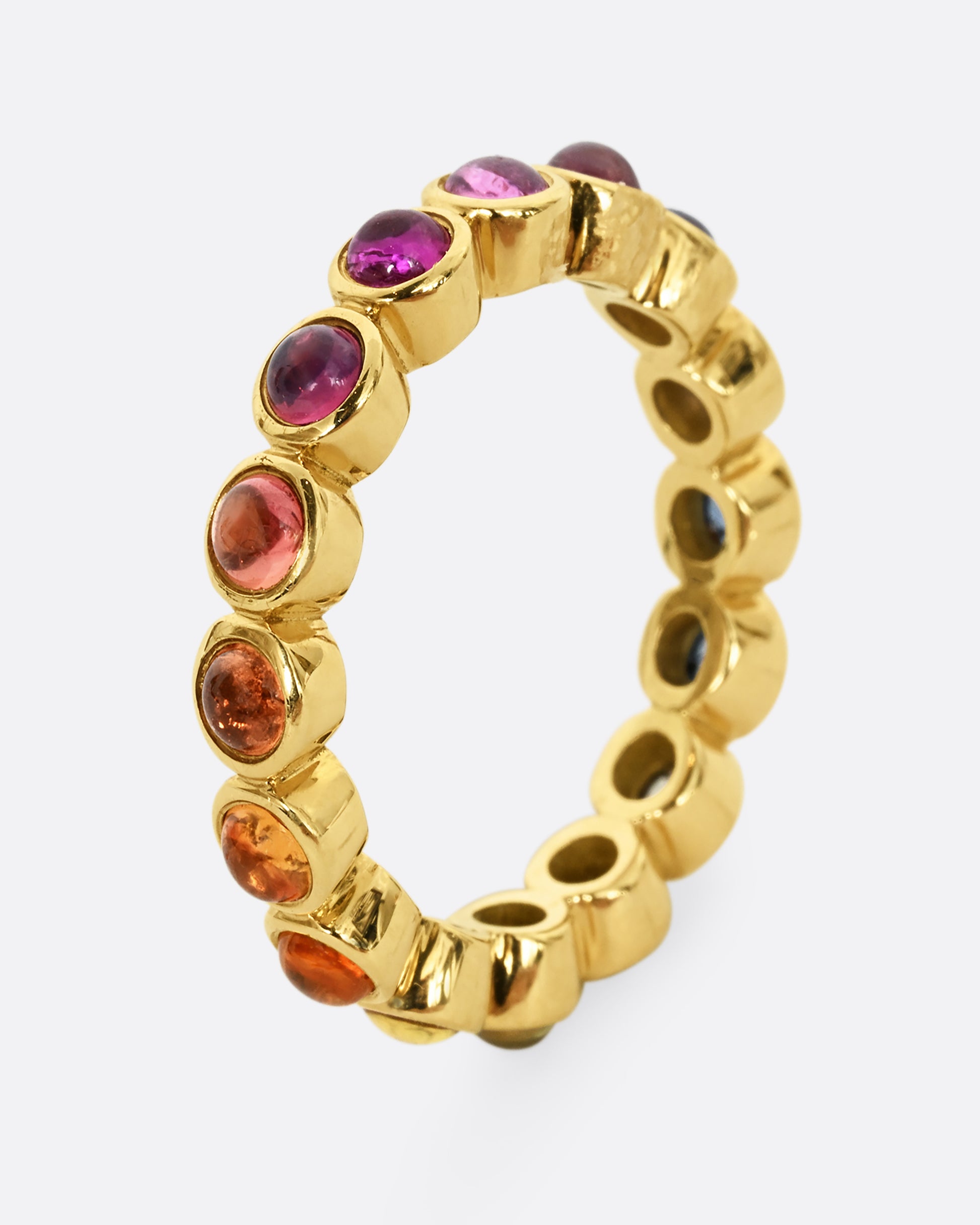 A yellow gold half eternity band with multicolor bezel set sapphire cabochons. Shown from the side, standing up.