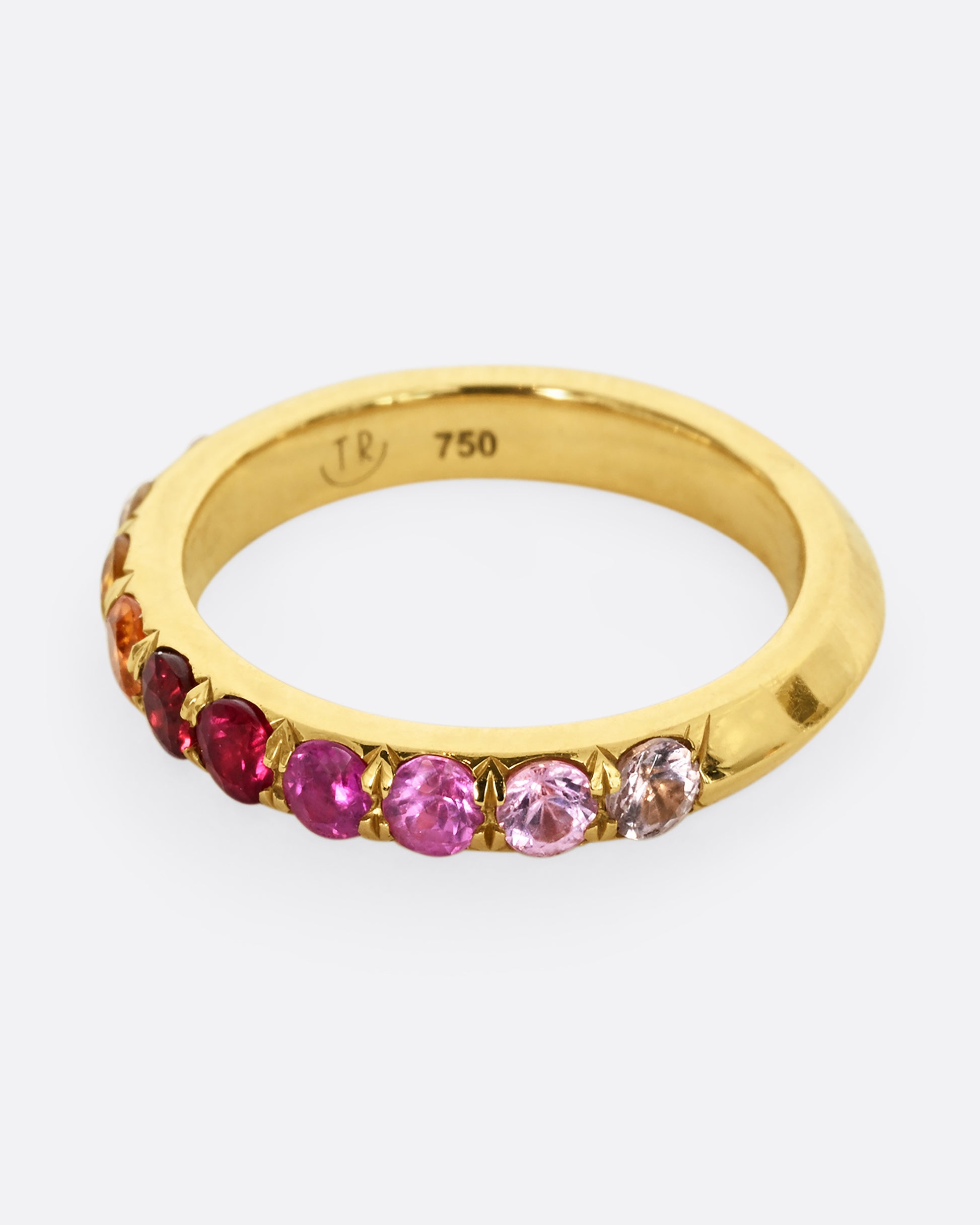 A yellow gold half eternity band with gradient orange red and pink cut sapphires. Shown from the side.