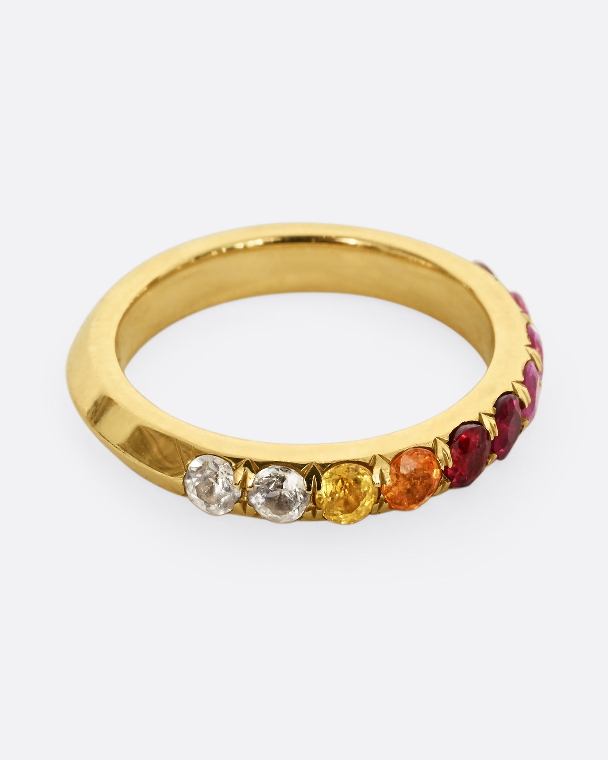 A yellow gold half eternity band with gradient orange red and pink cut sapphires. Shown from the side, from above.