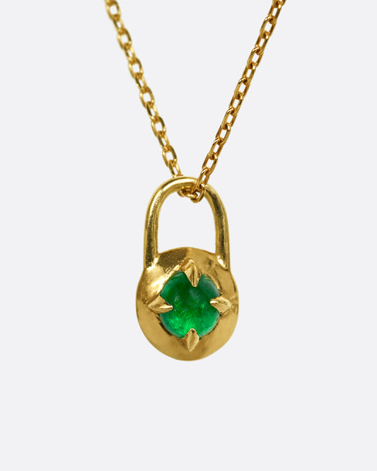 A yellow gold pendant in the shape of a lock with an emerald cabochon at the center. Shown styled on a chain.