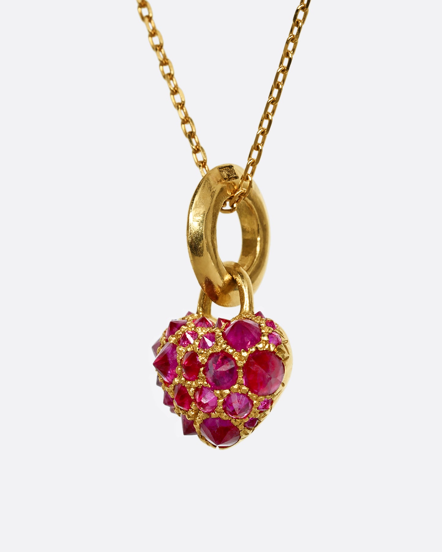 A yellow gold heart shaped charm with inverted rubies throughout. View from the side.