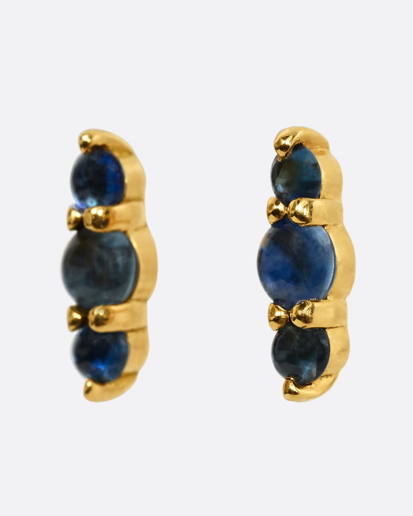 Stud earrings made of three blue sapphire cabochons set in yellow gold. Shown from the side.