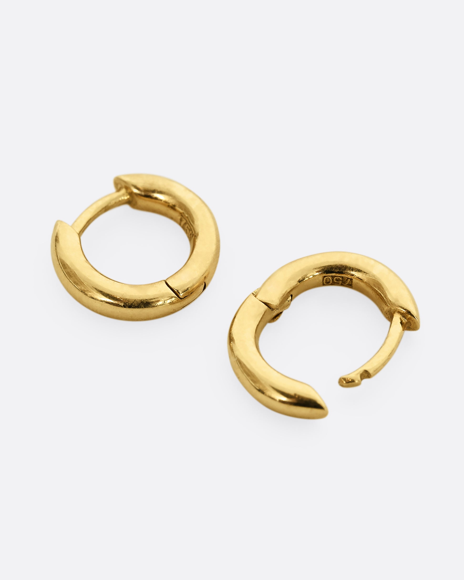 Yellow gold huggie hoops, shown laying flat.